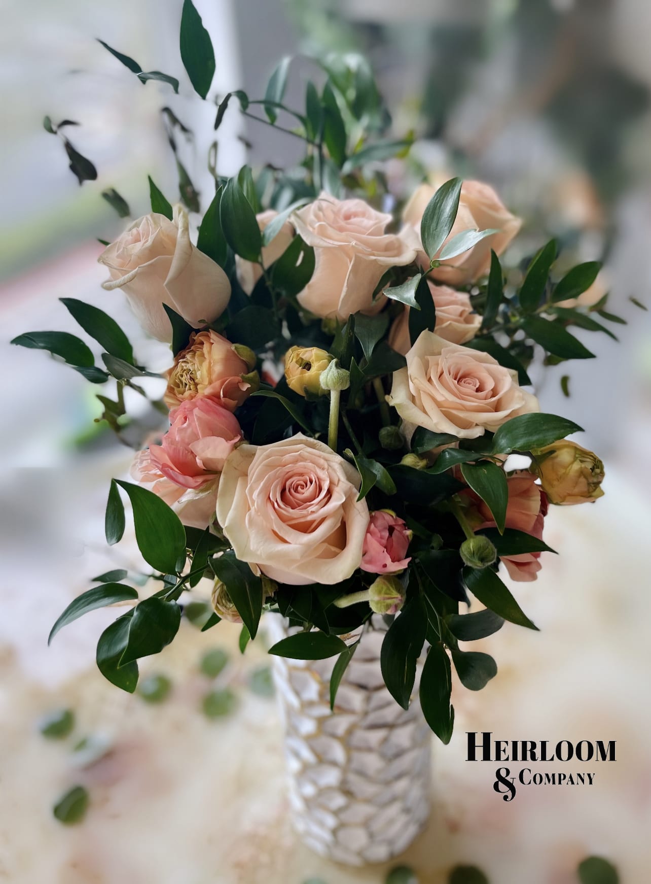 Blush roses arranged in a textured white vase with dark foliage