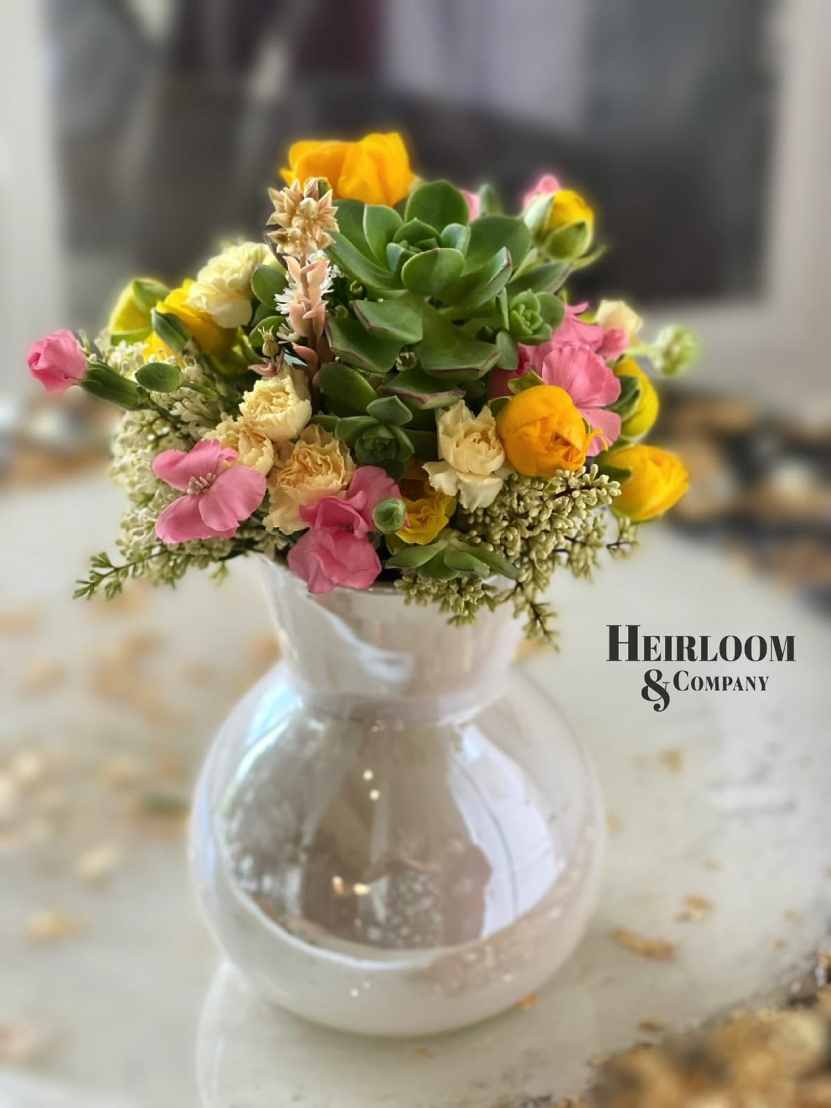 Mixed pink and yellow flowers in a clear glass vase with succulents