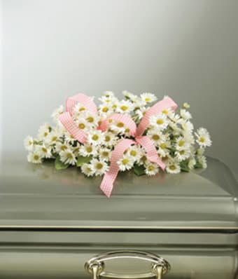 White daisy arrangement with pink ribbon on a casket