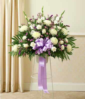 White and purple floral spray on a clear stand with a lavender ribbon