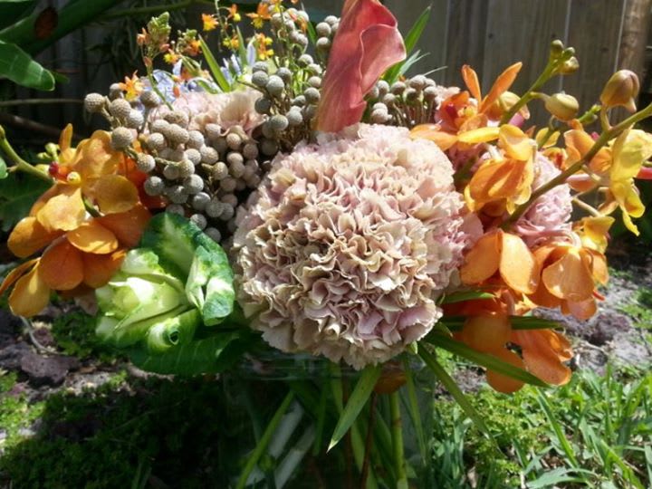 Cluster Buster - Large Clusters of Antique Carnations, Orange Makara Orchids, Variegated Kale, Brunia Berries, Oncidium Orchids, Mango Calla Lillies designed into a clear glass vase