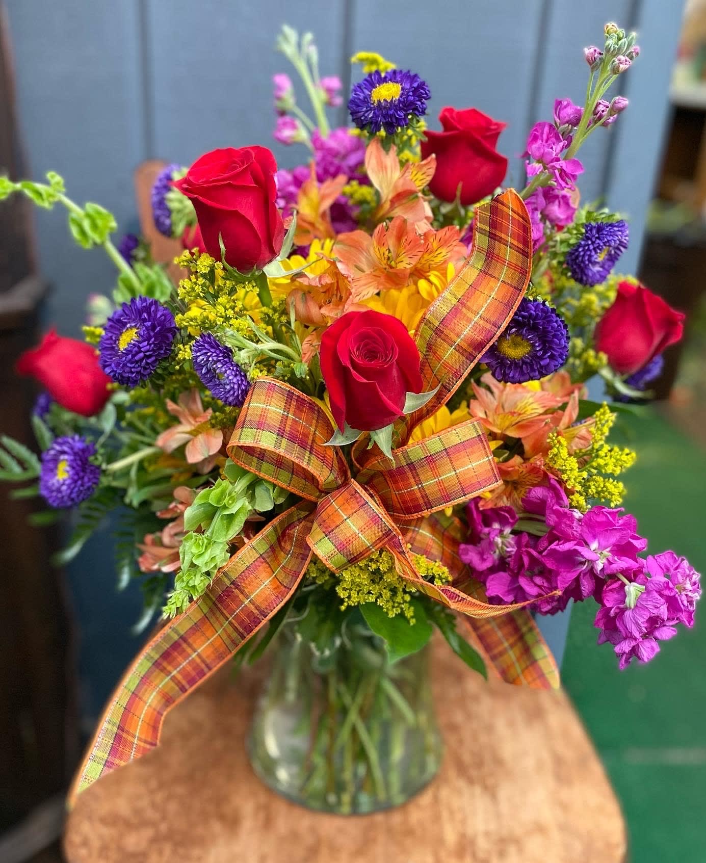 Fall Hues Bouquet - A nice mix of fresh flowers in some of the best fall hues designed in a clear vase and finished off with a plaid fall toned bow. 