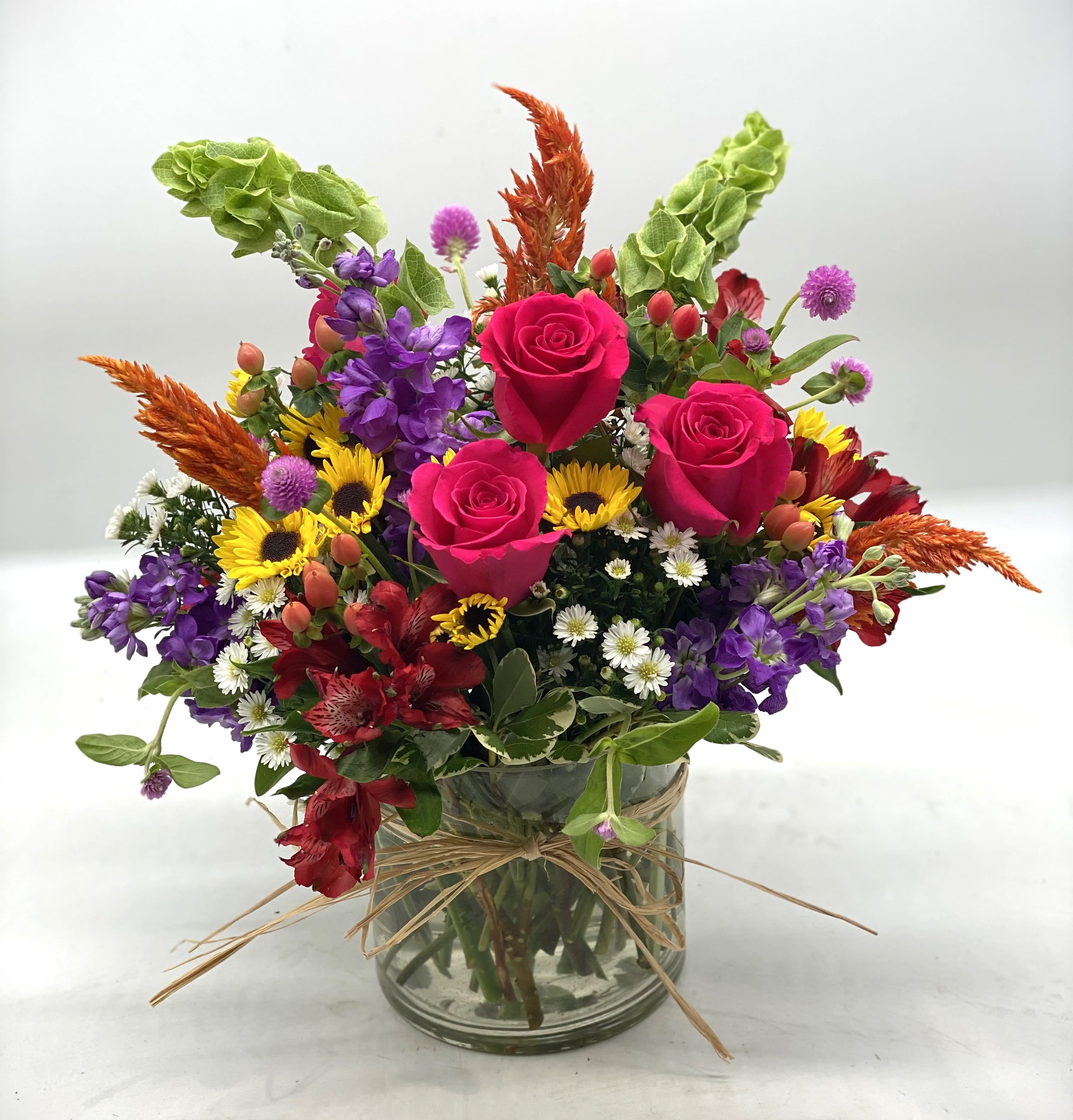 Mixed bouquet of pink roses, purple flowers, and sunflowers in a glass vase