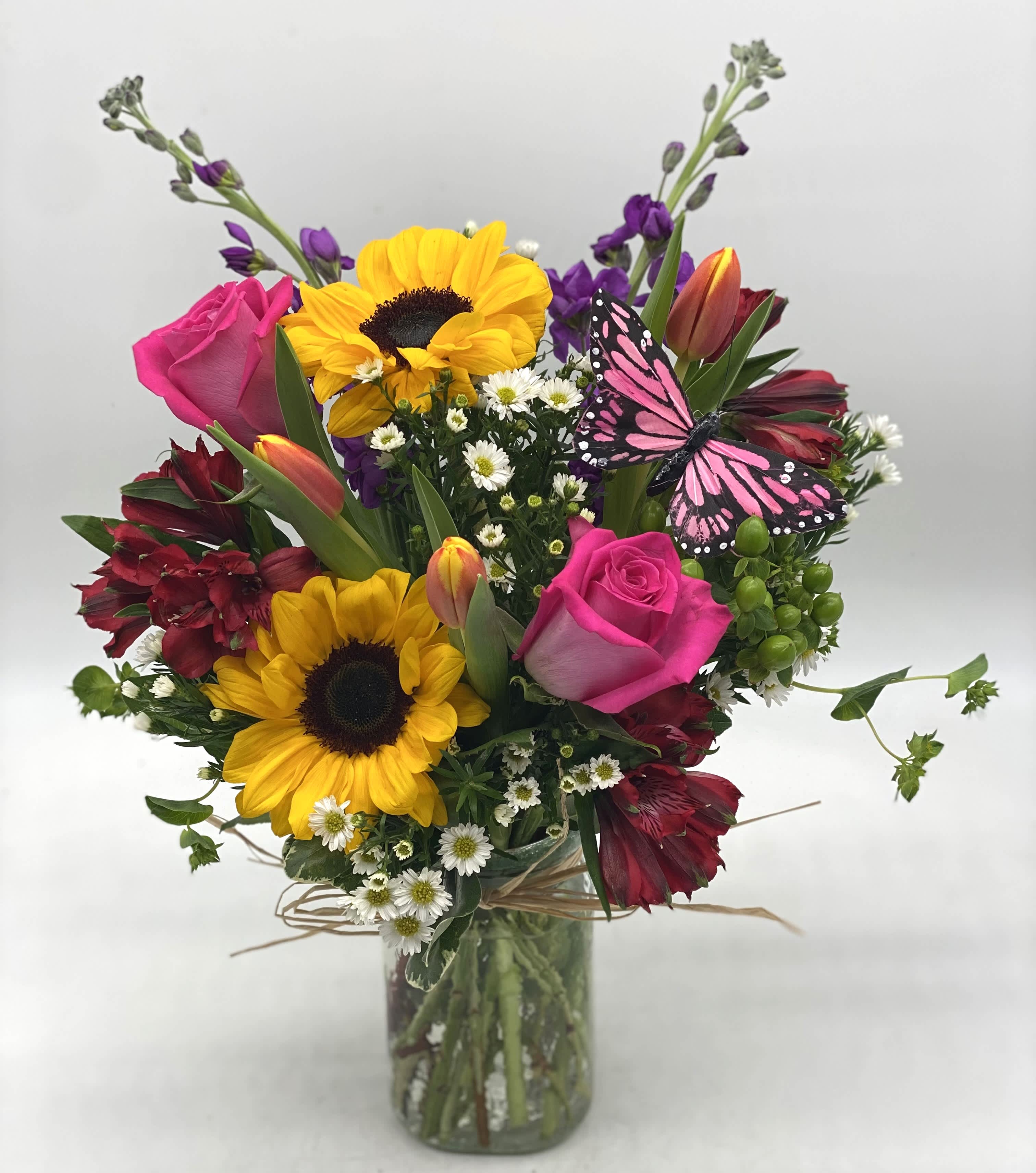 Mixed bouquet with sunflowers, pink roses, and a butterfly in a glass vase