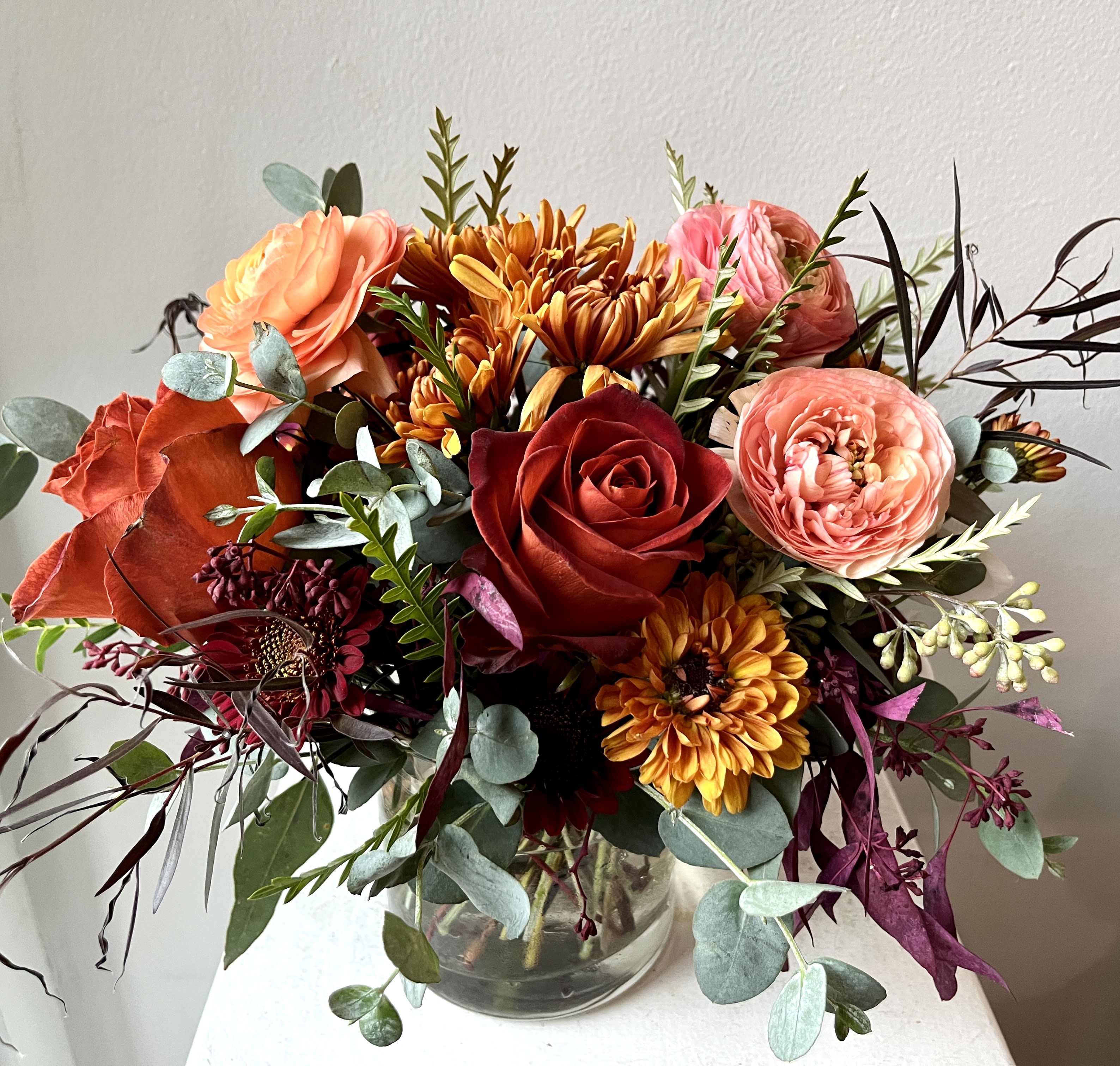 Mixed bouquet of roses, ranunculus, and chrysanthemums in a glass vase