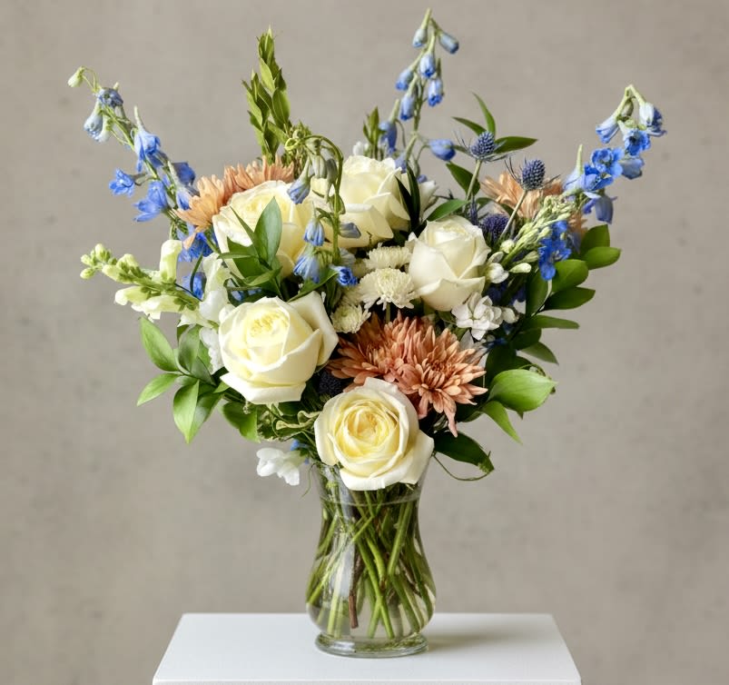 Bouquet of white roses, blue flowers, and peach blooms in a clear glass vase