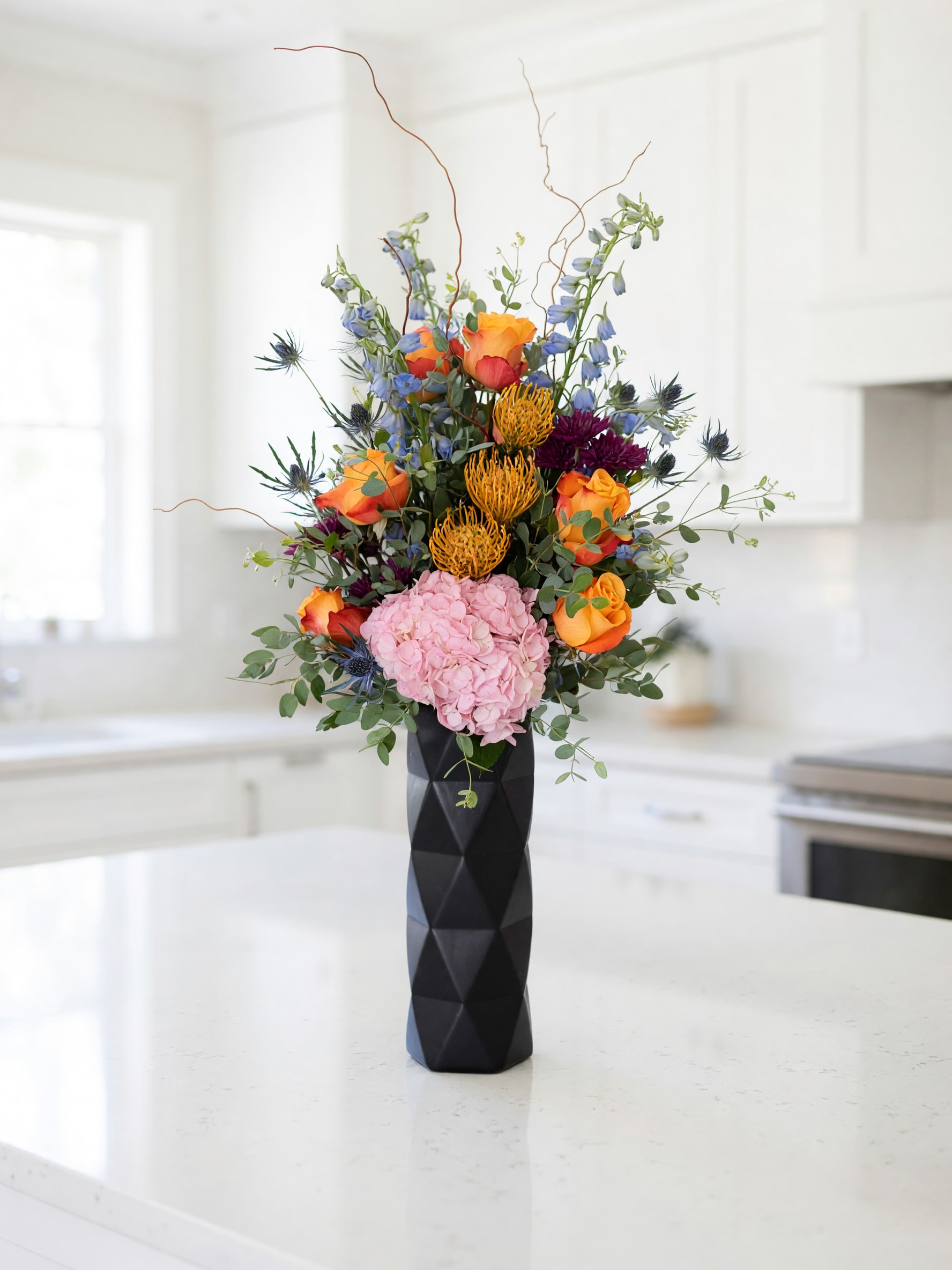 Tall bouquet of orange and pink flowers in a black vase