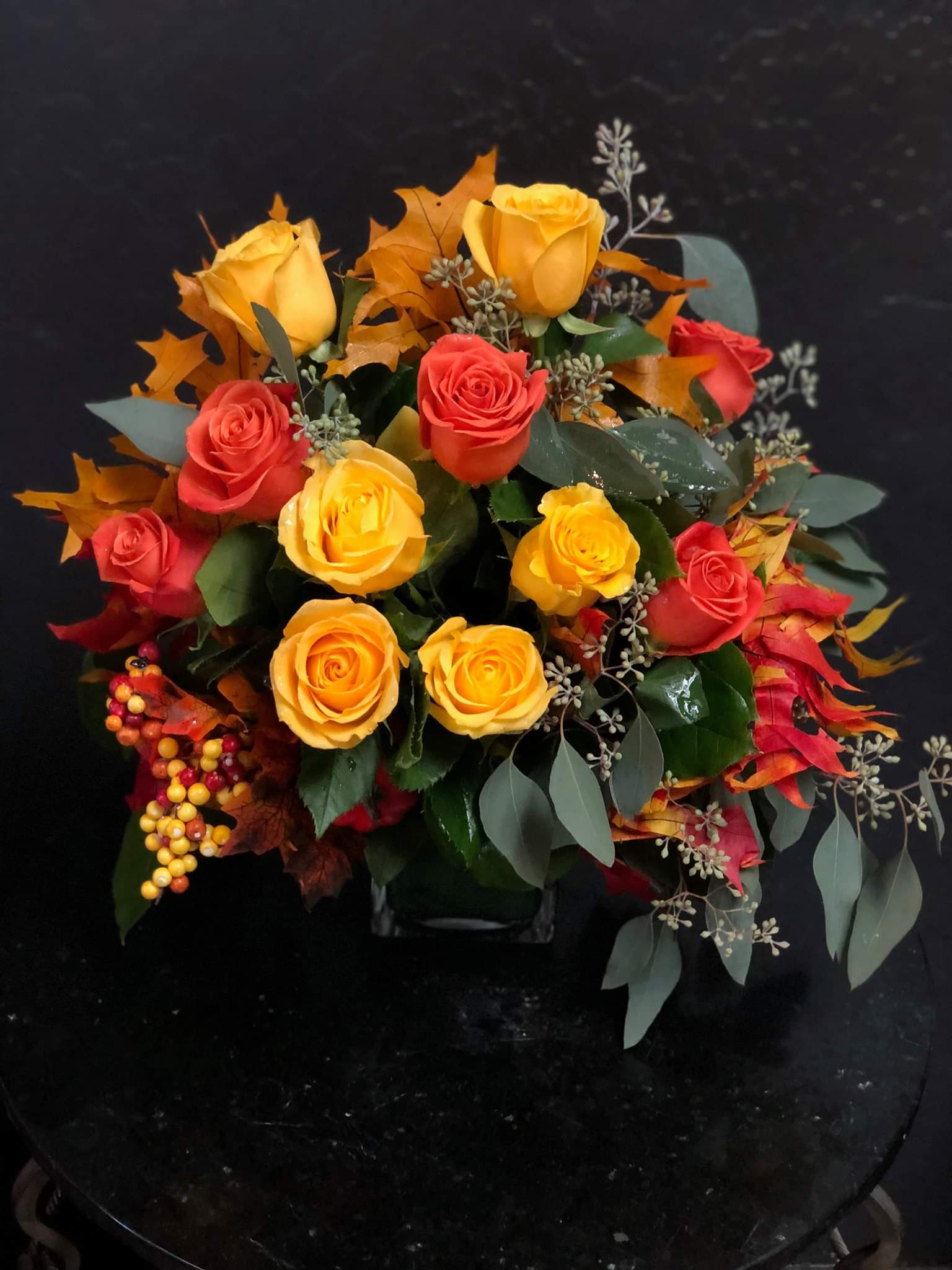 Bouquet of yellow and red roses with autumn leaves in a vase