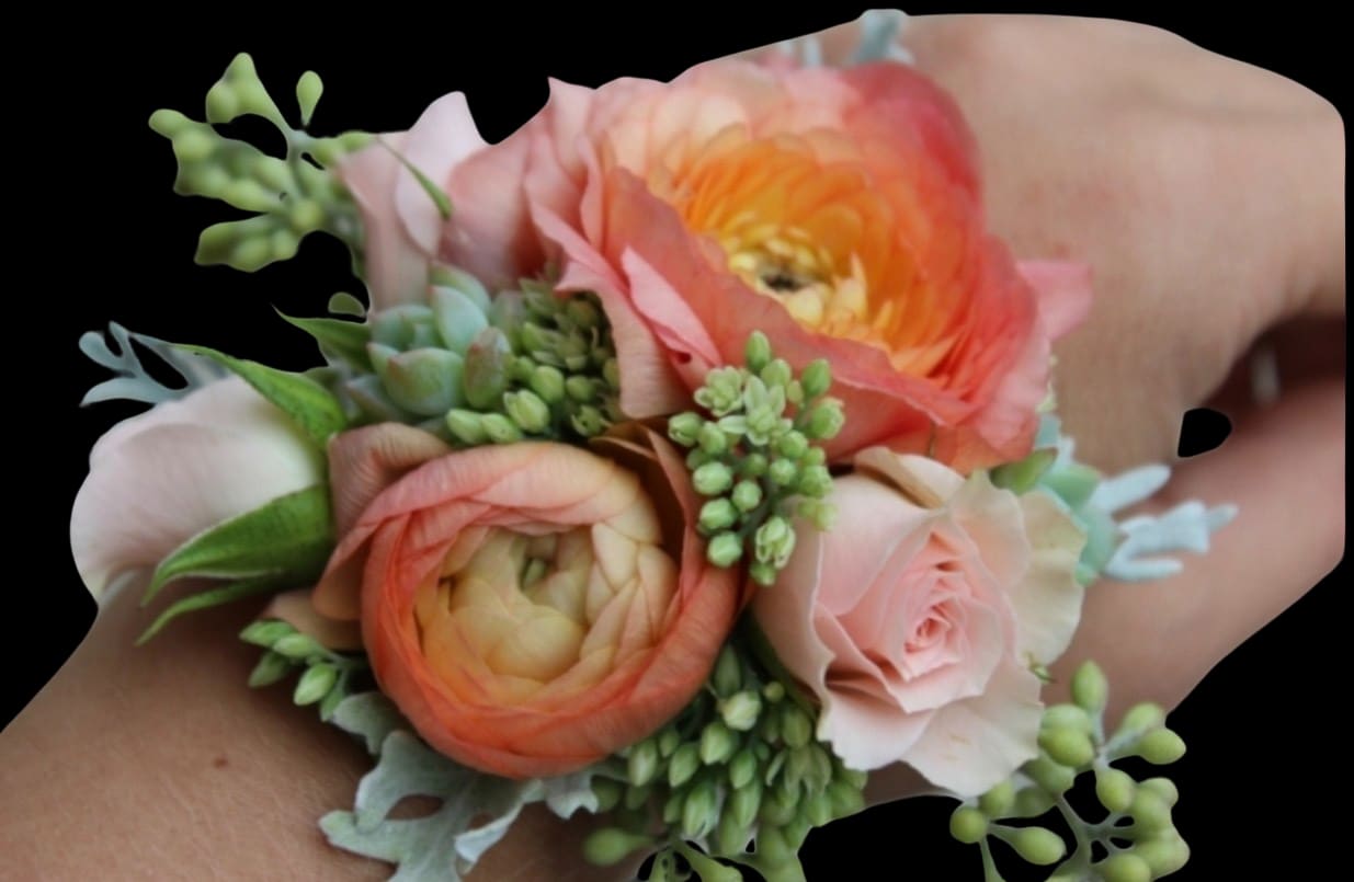 Corsage with peach and pink flowers and green accents on a wrist