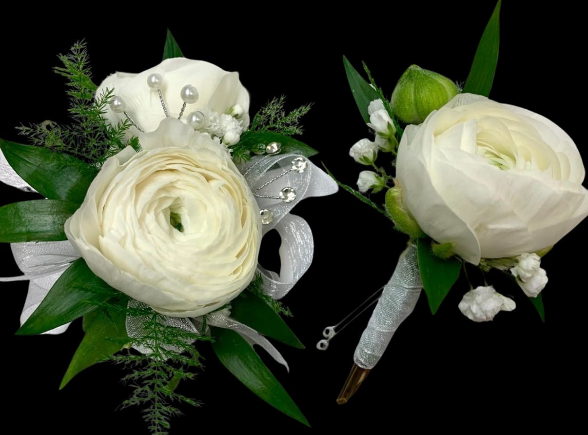 Two white floral boutonnieres with ribbon and pearl accents on a black background