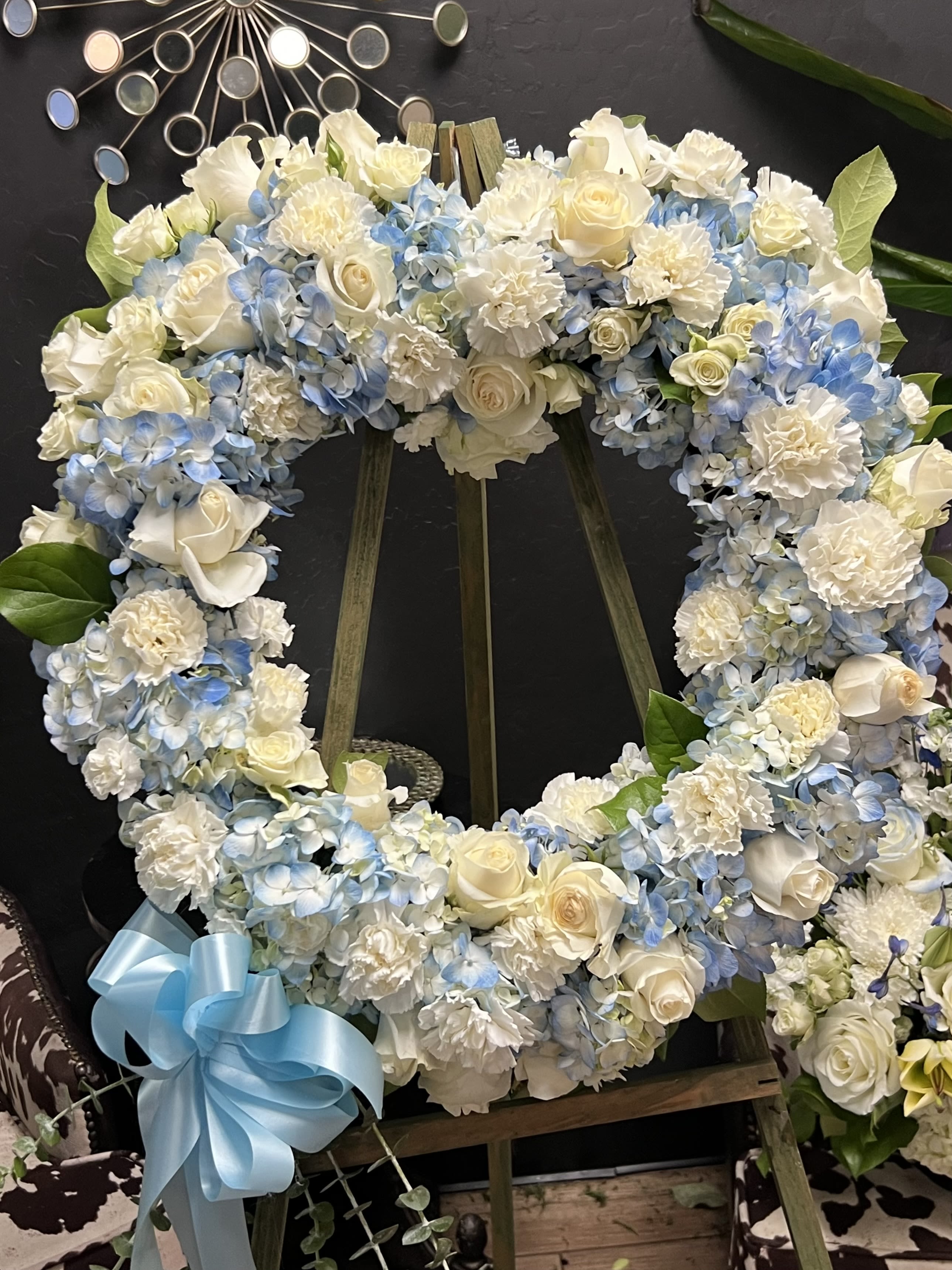 Heart-shaped floral wreath with white roses and blue hydrangeas on an easel