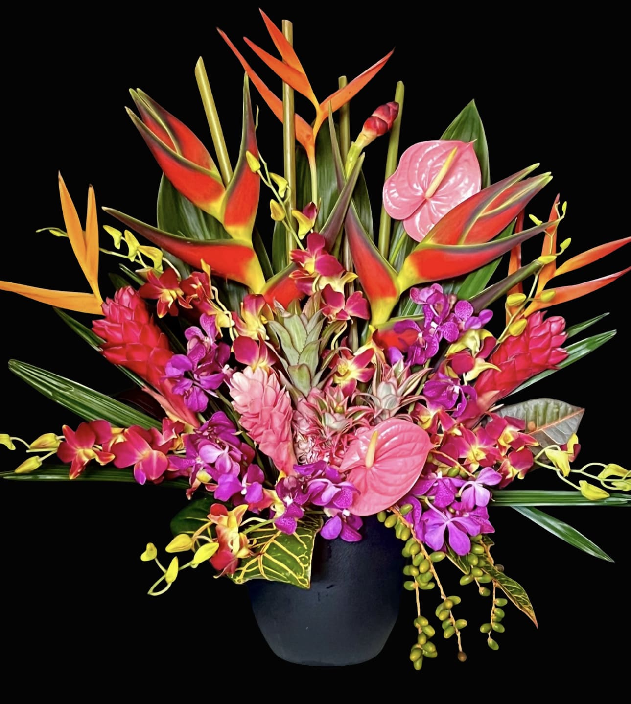 Tropical flower arrangement in a black vase with pink anthuriums and orchids