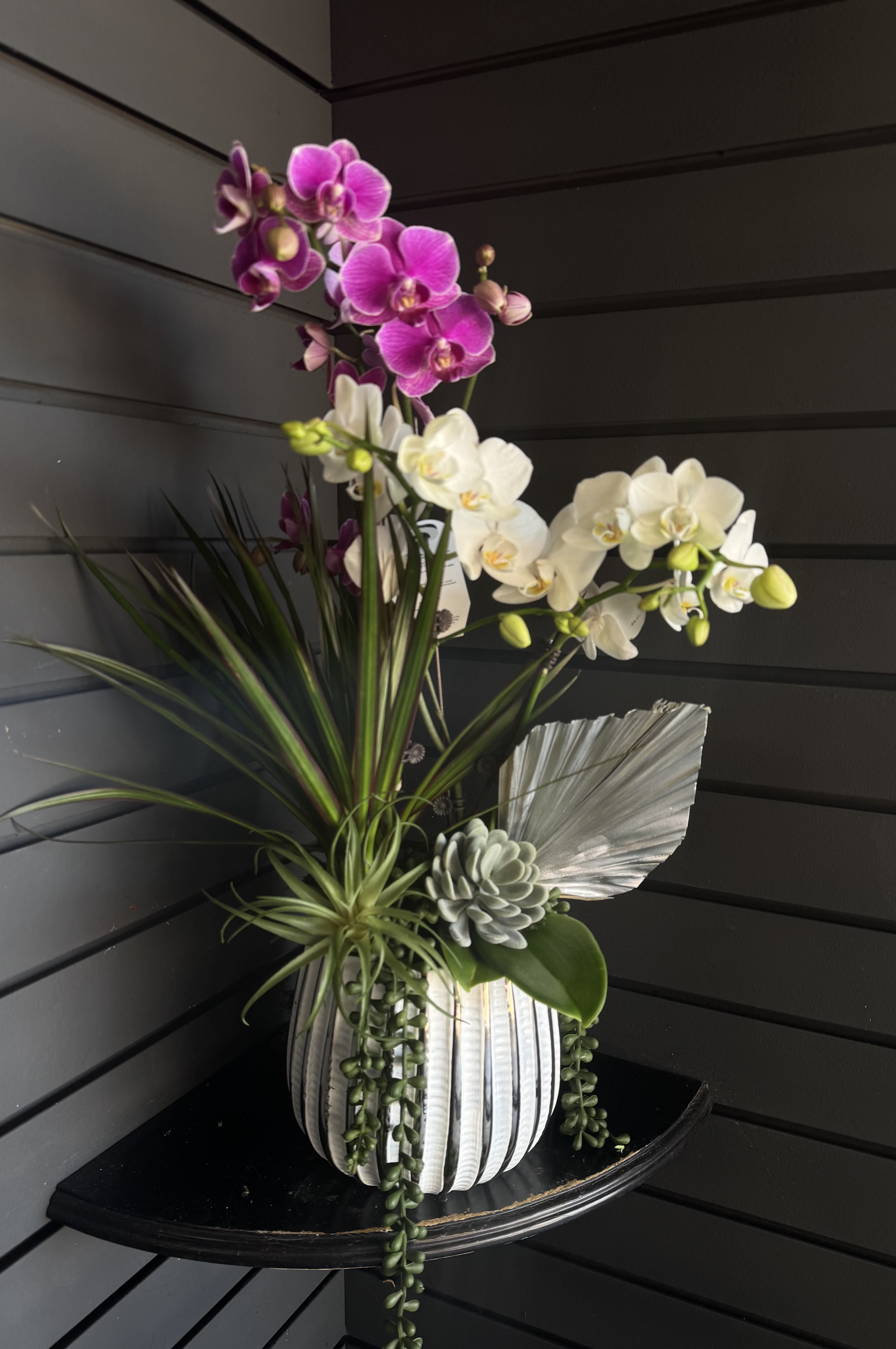 Orchid arrangement in a ribbed white vase with succulents and decorative leaves