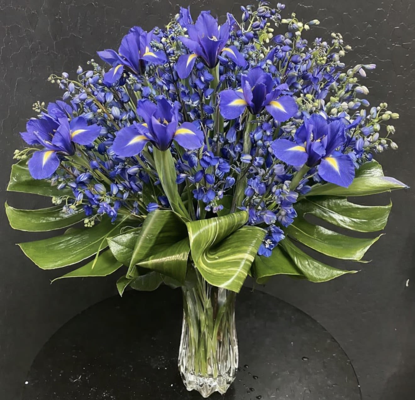 Blue iris bouquet in a clear glass vase with broad green leaves