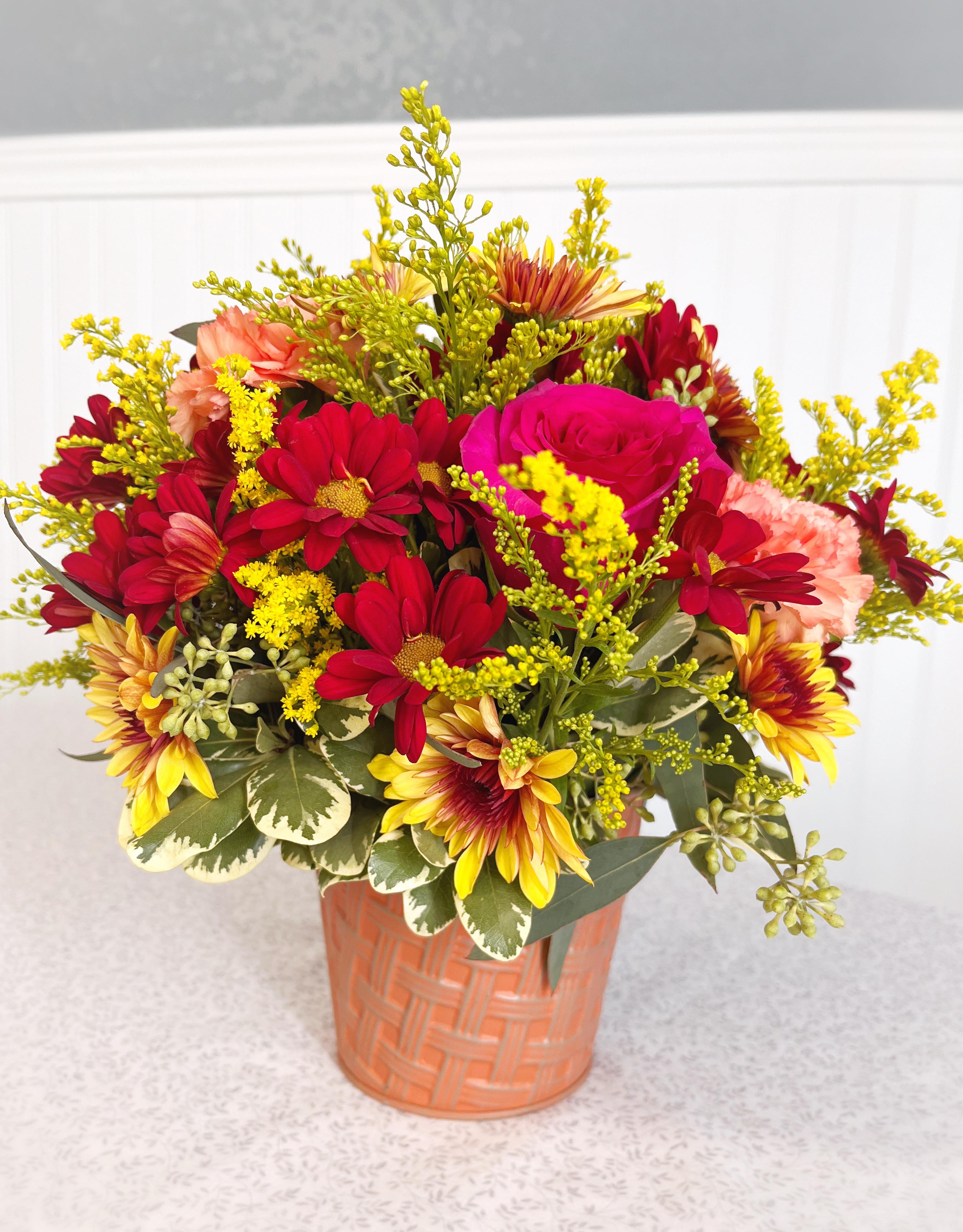 Mixed bouquet of red, pink, and yellow flowers in a peach basket vase