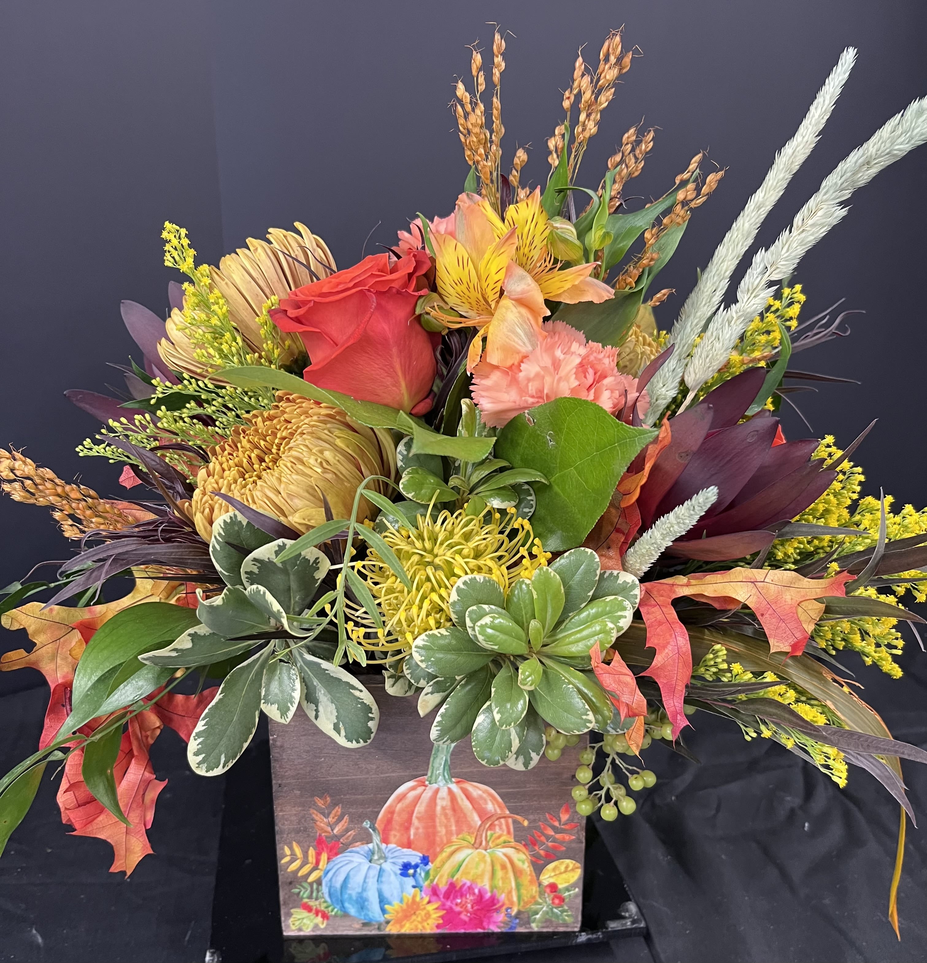 Autumn floral arrangement in a painted pumpkin box with red, yellow, and peach blooms