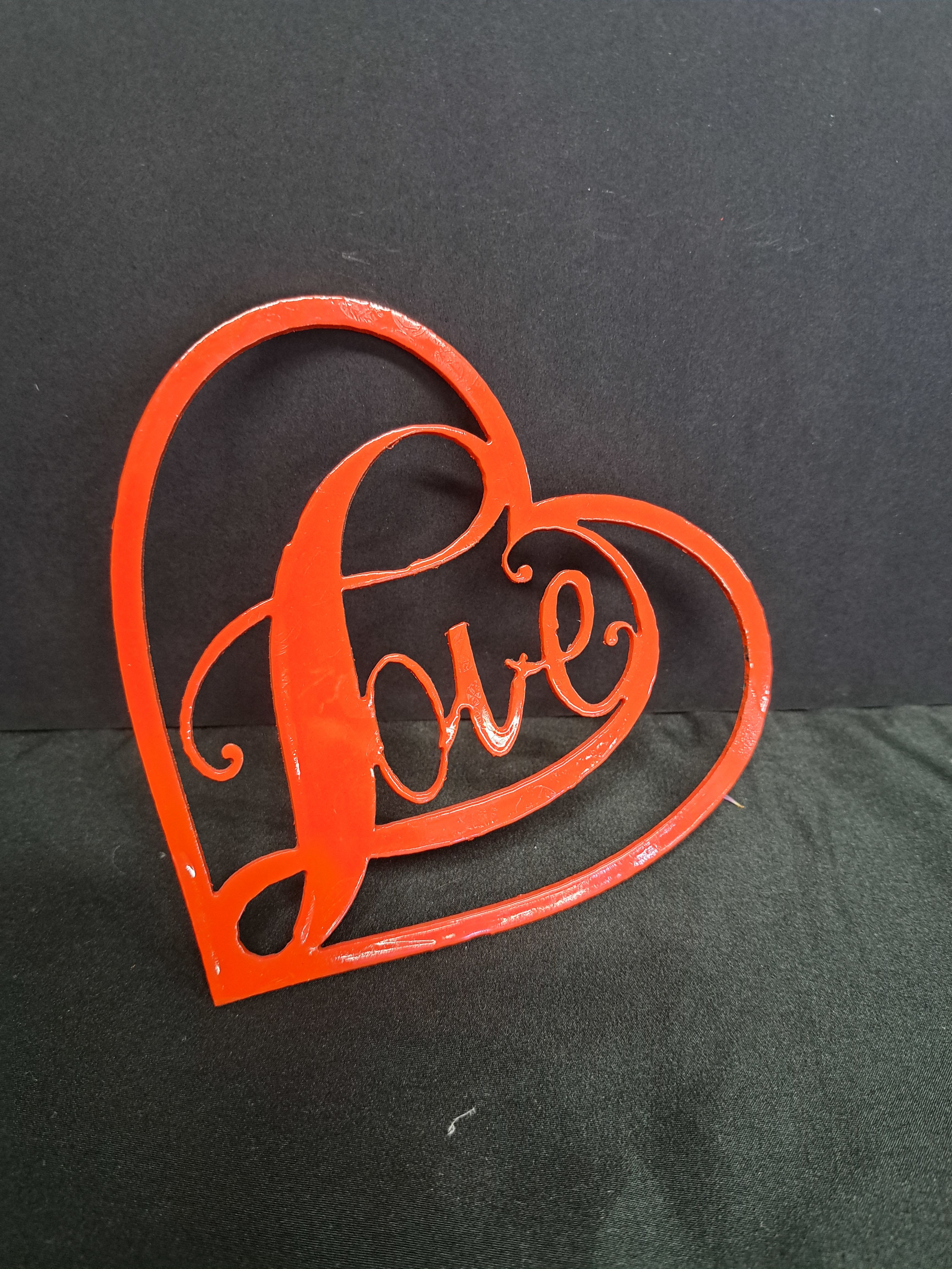 Metal Heart wall hanger Fancy Love - A glossy red metal heart with the word love cut into its center makes a bold, romantic statement-perfect as a small gift or accent for Valentine's Day, an anniversary, or any love-themed celebration. This metal heart wall hanger reads clearly from across the room; the playful script and high-contrast red-on-black look create an instant focal point that makes the person you're thinking of feel adored. 