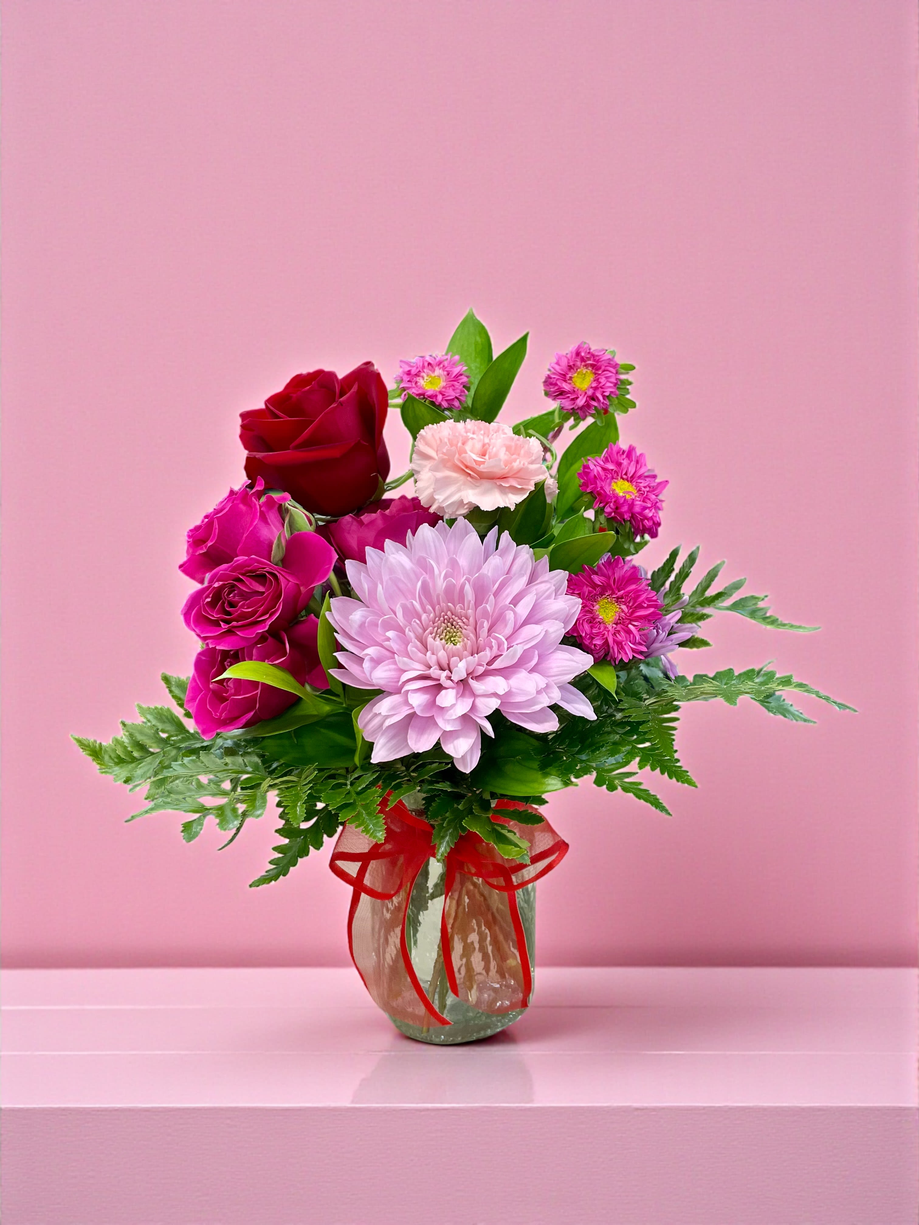 Bouquet of pink and red flowers in a glass vase with a red ribbon
