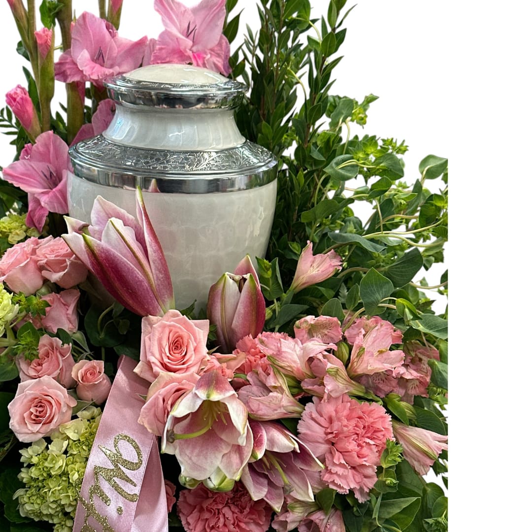 Pink flowers arranged around a silver urn with a pink ribbon