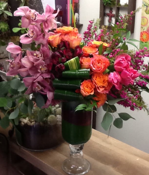 Mixed bouquet with pink orchids, orange roses, and magenta flowers in a glass vase