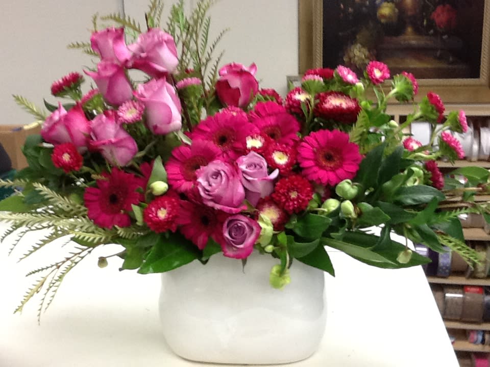 Pink roses and magenta daisies arranged in a white vase
