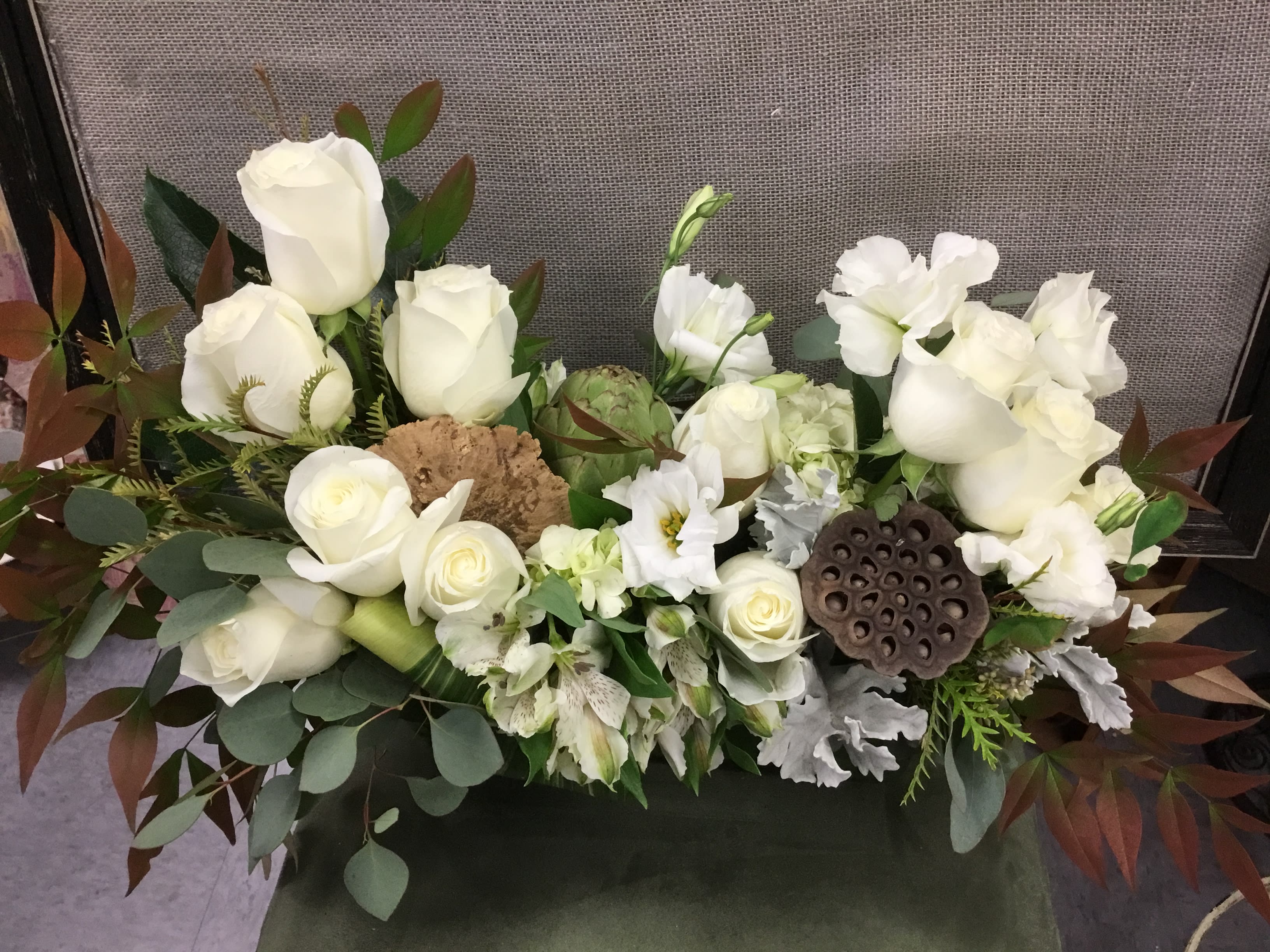 White roses and white blooms arranged with greenery in a low centerpiece