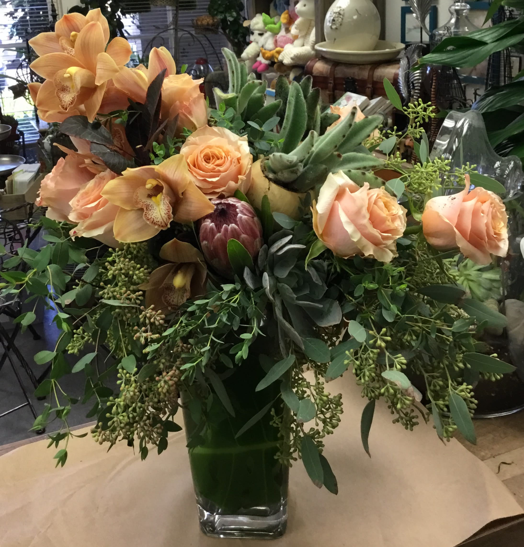 Peach roses and orchids in a glass vase with lush greenery