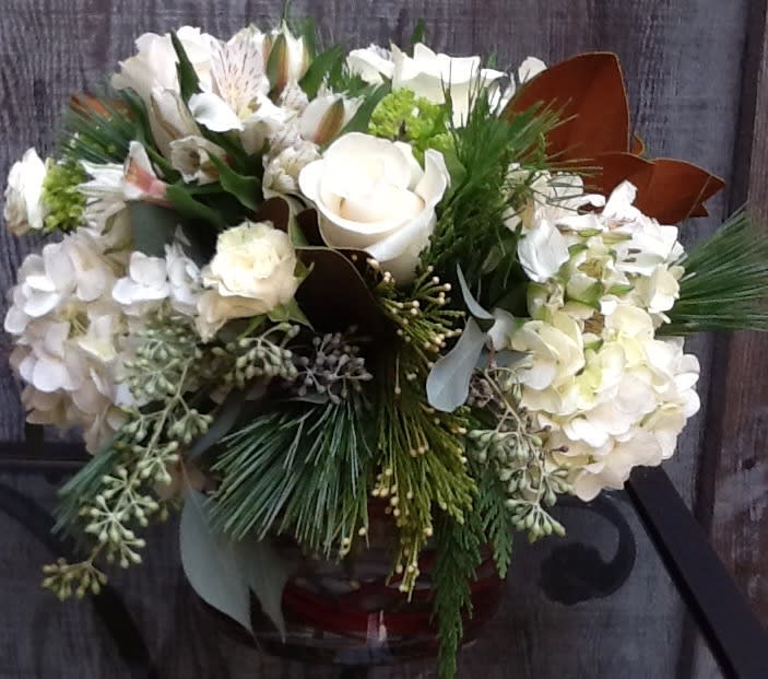 White floral arrangement in a glass vase with pine accents