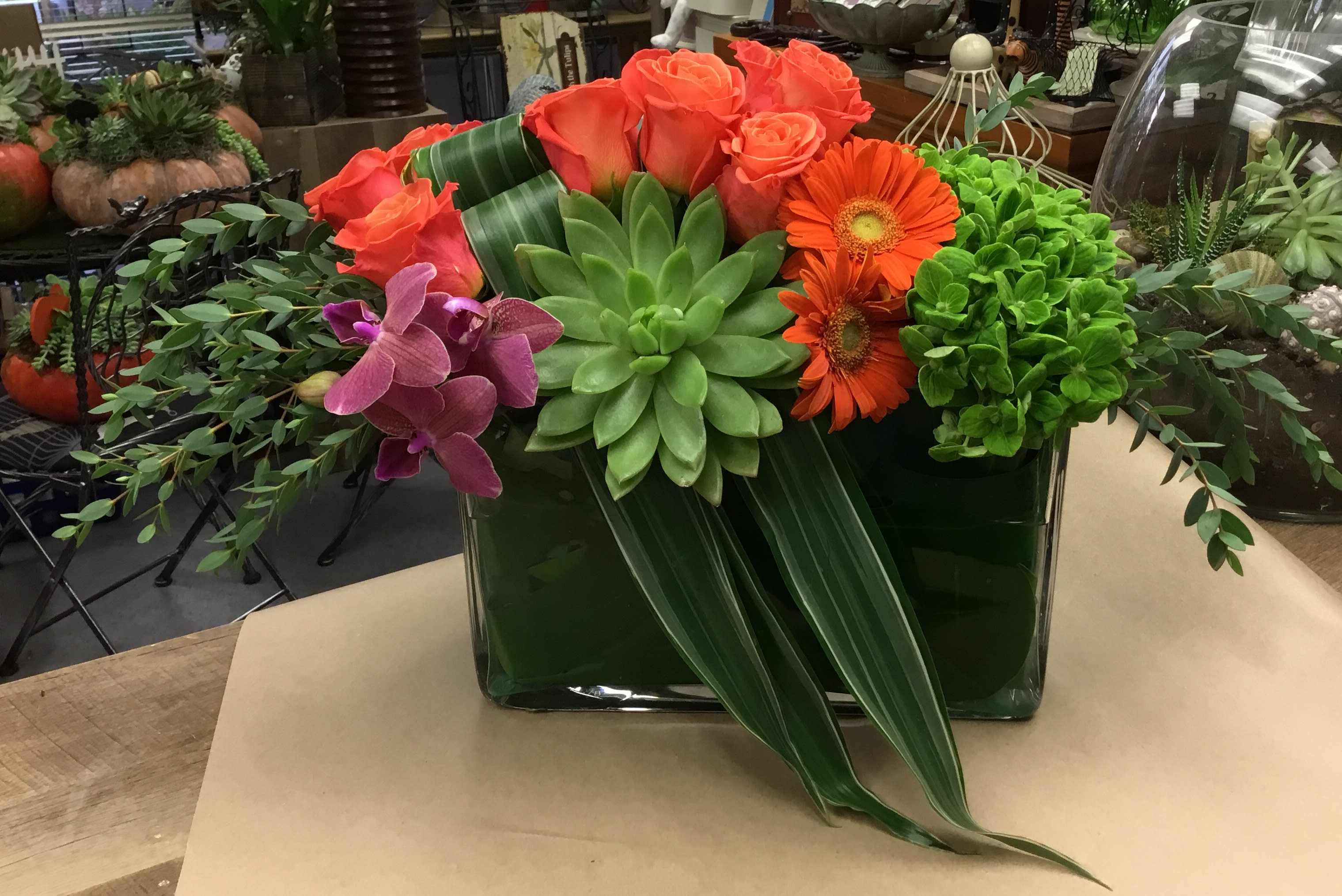 Succulent and rose arrangement with orange gerbera daisies in a glass vase