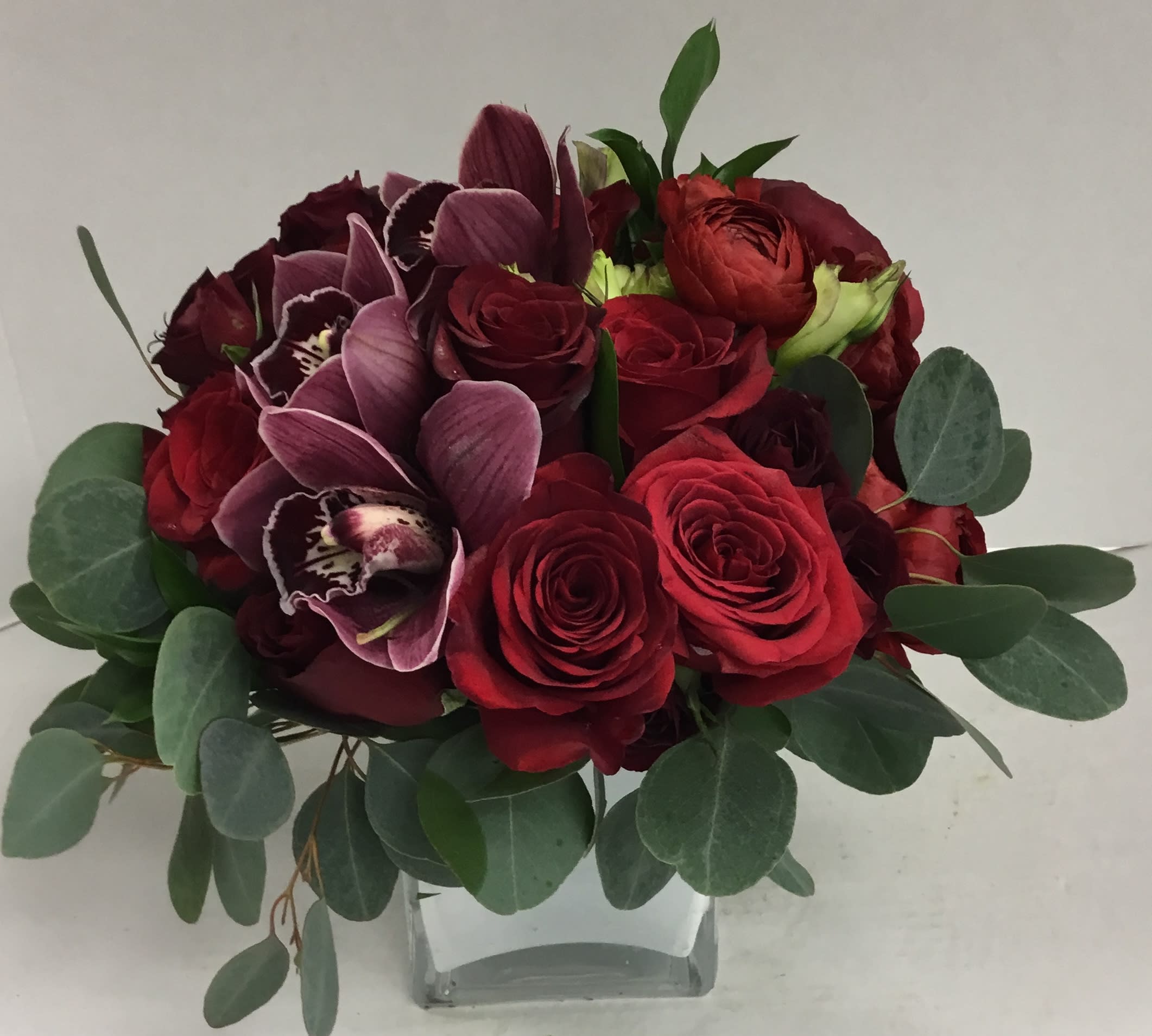 Red roses and purple orchids in a clear glass vase with eucalyptus