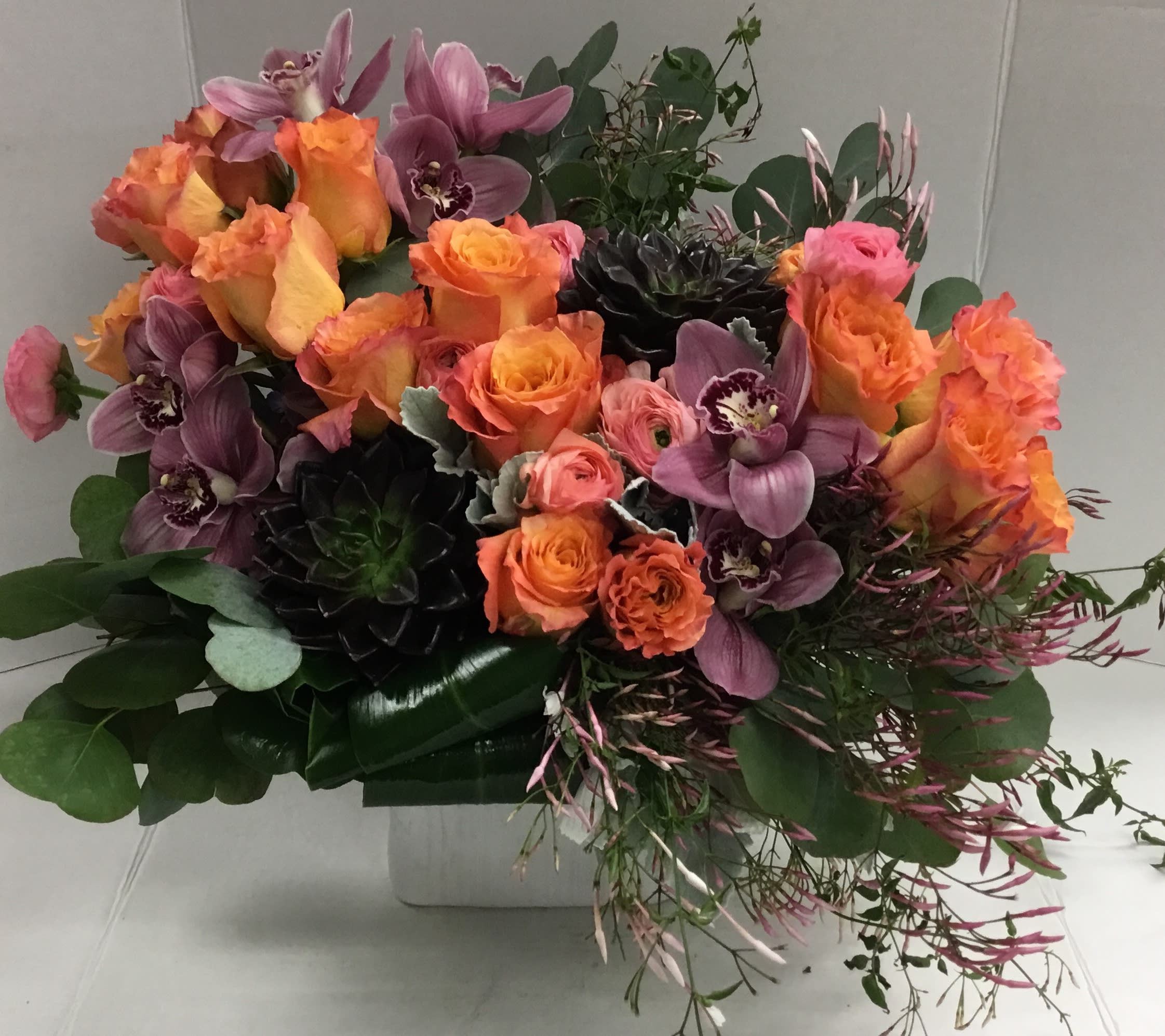 Bouquet of orange roses and purple orchids in a white container