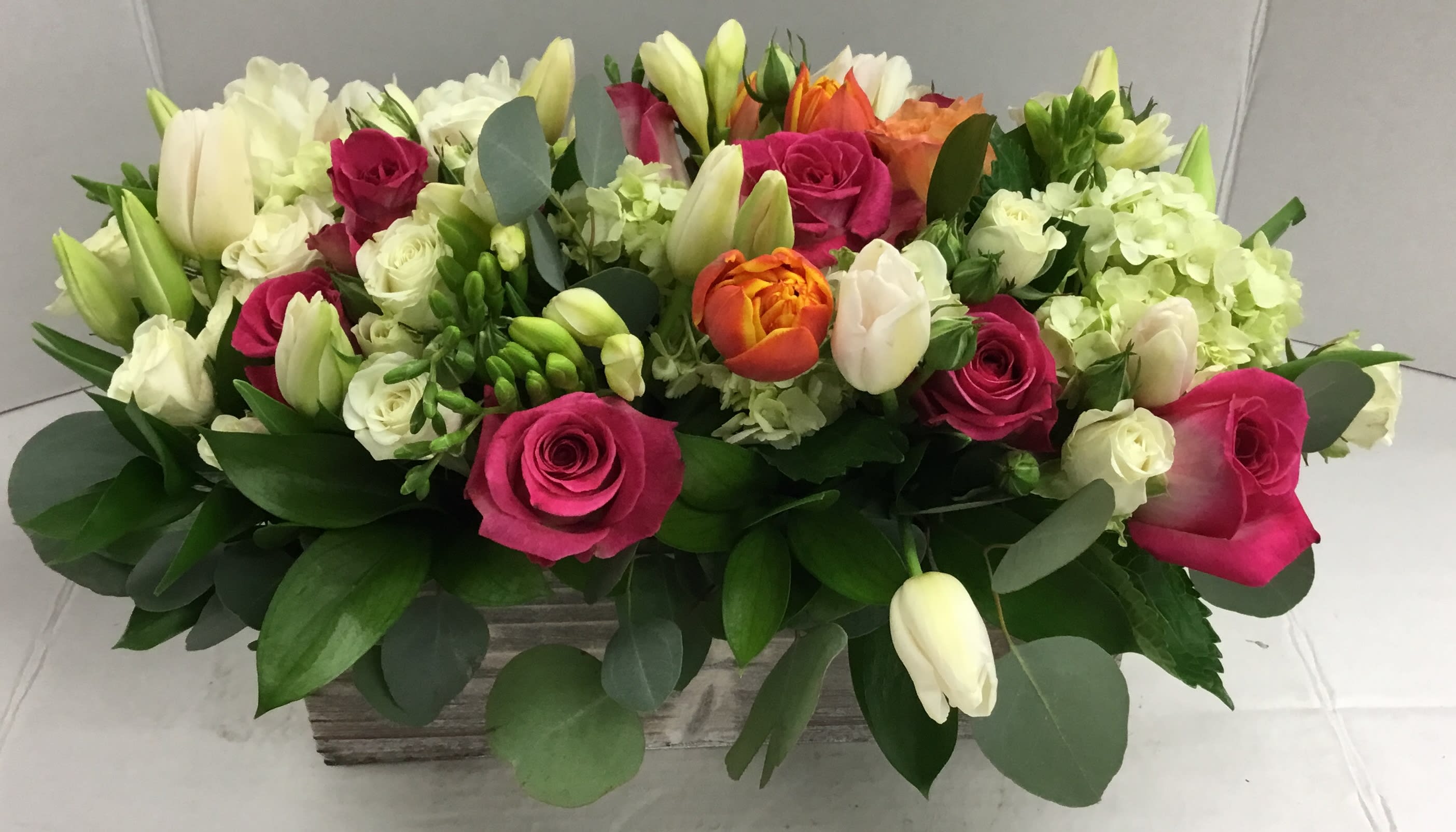 Mixed bouquet of pink roses, white tulips, and pale hydrangeas in a rectangular container