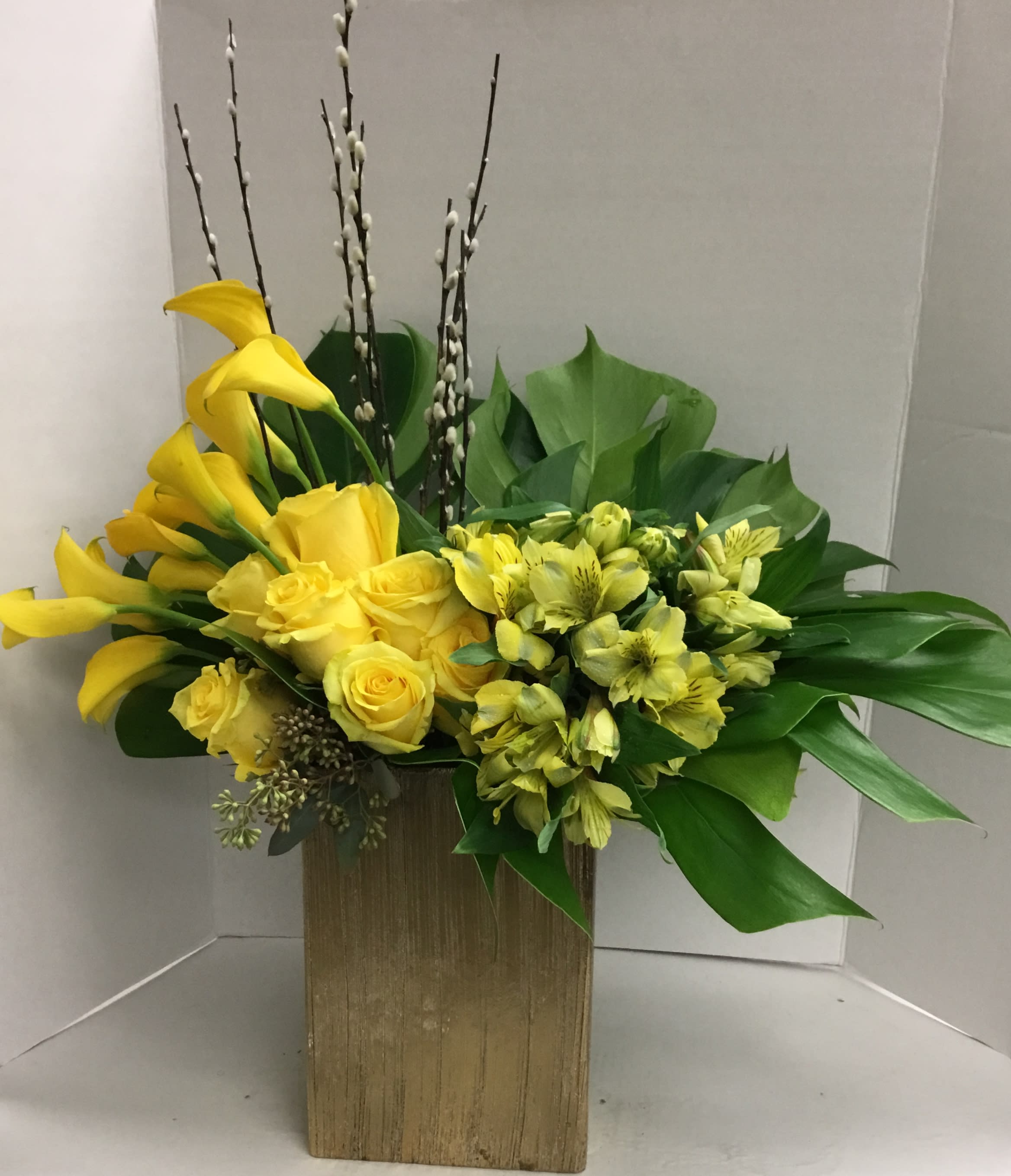 Yellow calla lilies and roses in a gold rectangular vase