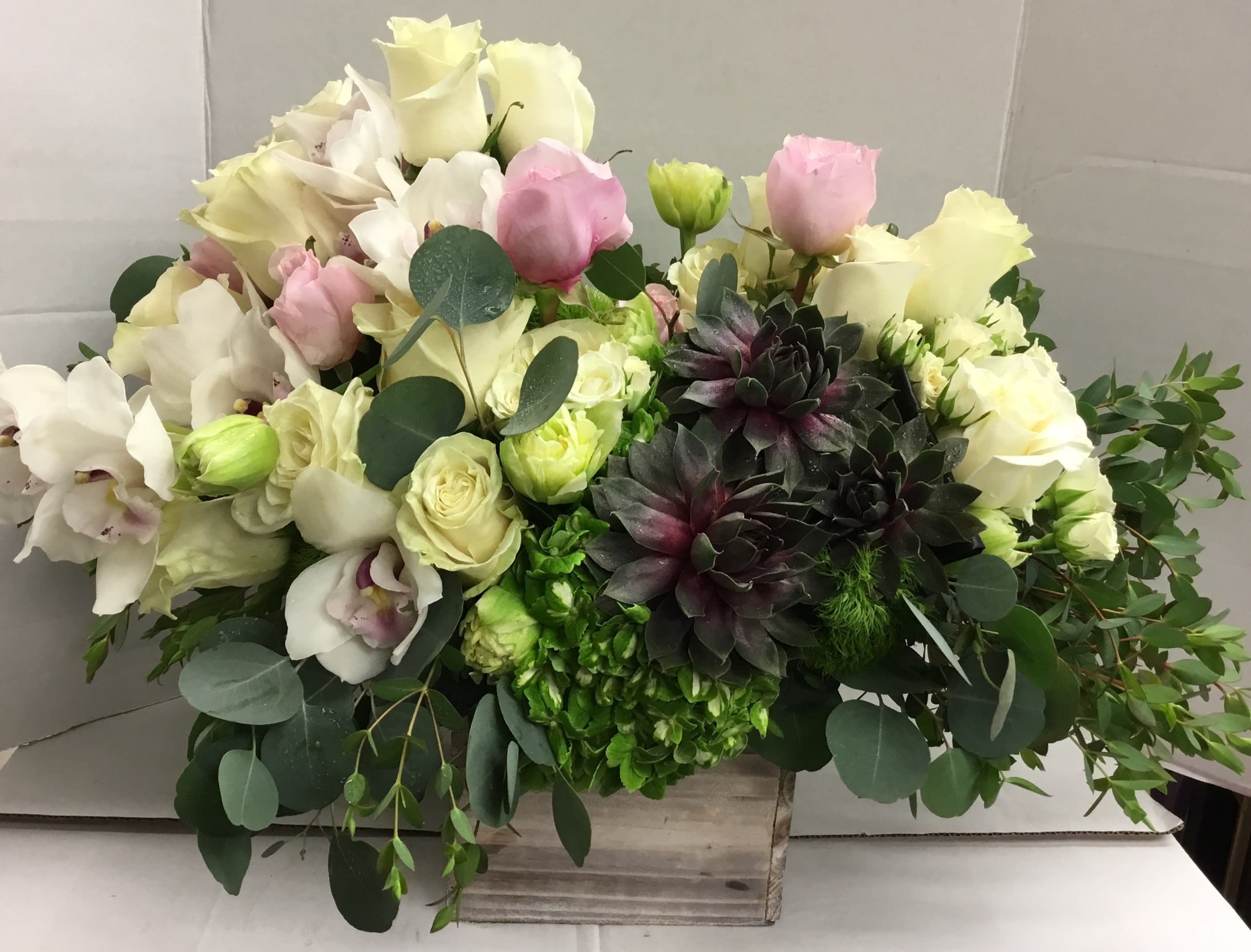 Mixed bouquet of white and pink roses with dark succulents in a wooden box