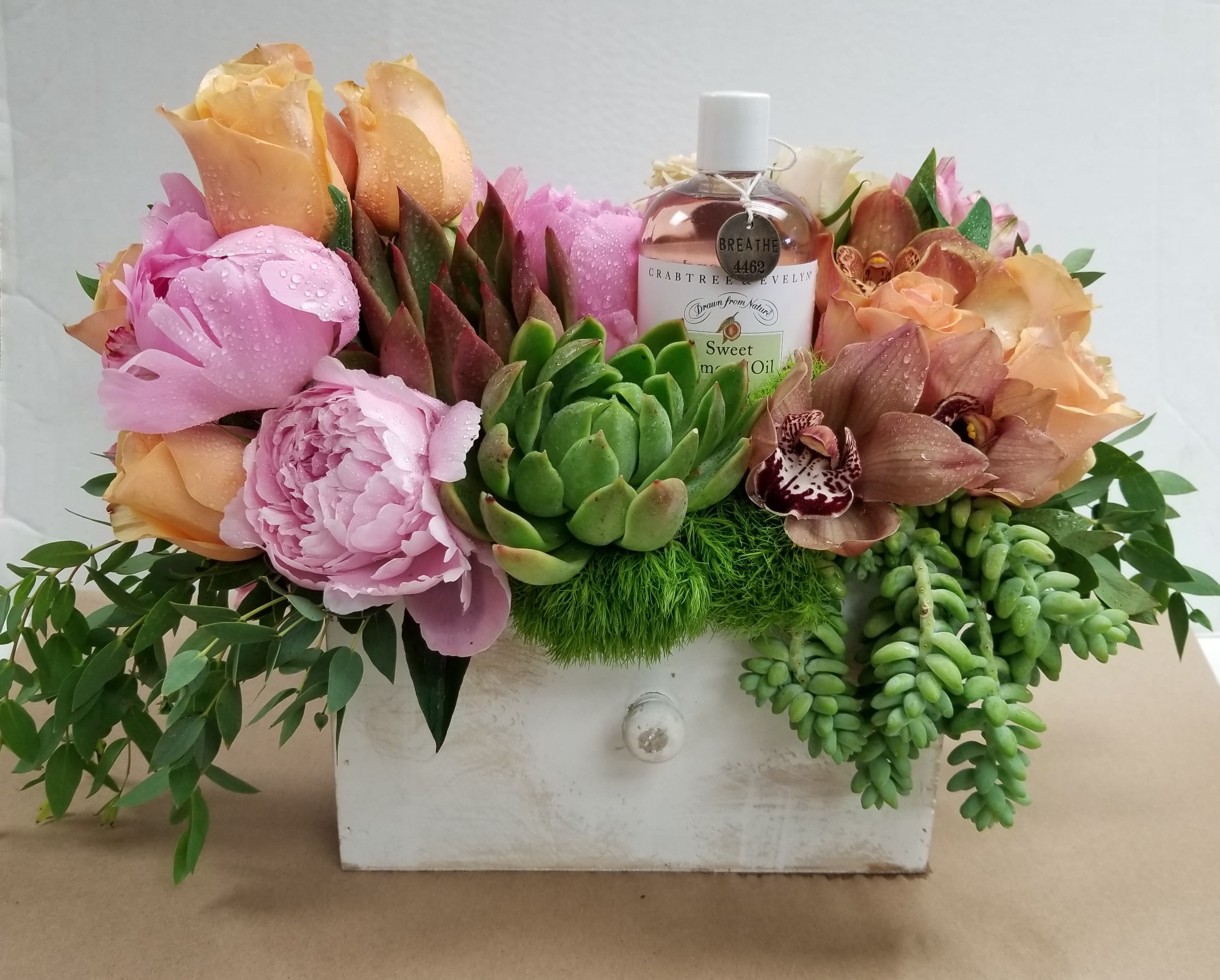 Flower arrangement in a white drawer box with a bottle of sweet almond oil