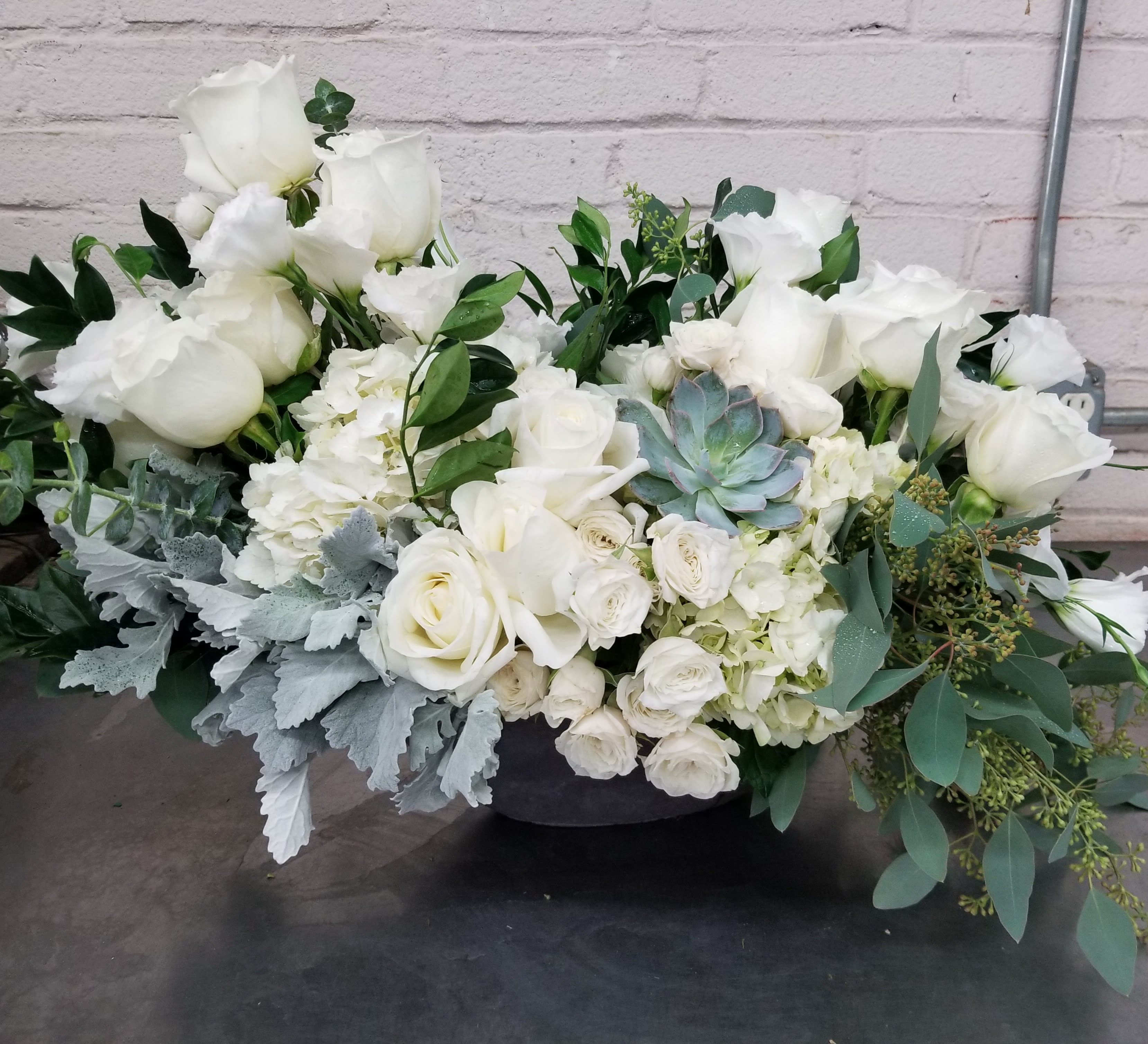 White rose arrangement with succulents and greenery in a low container