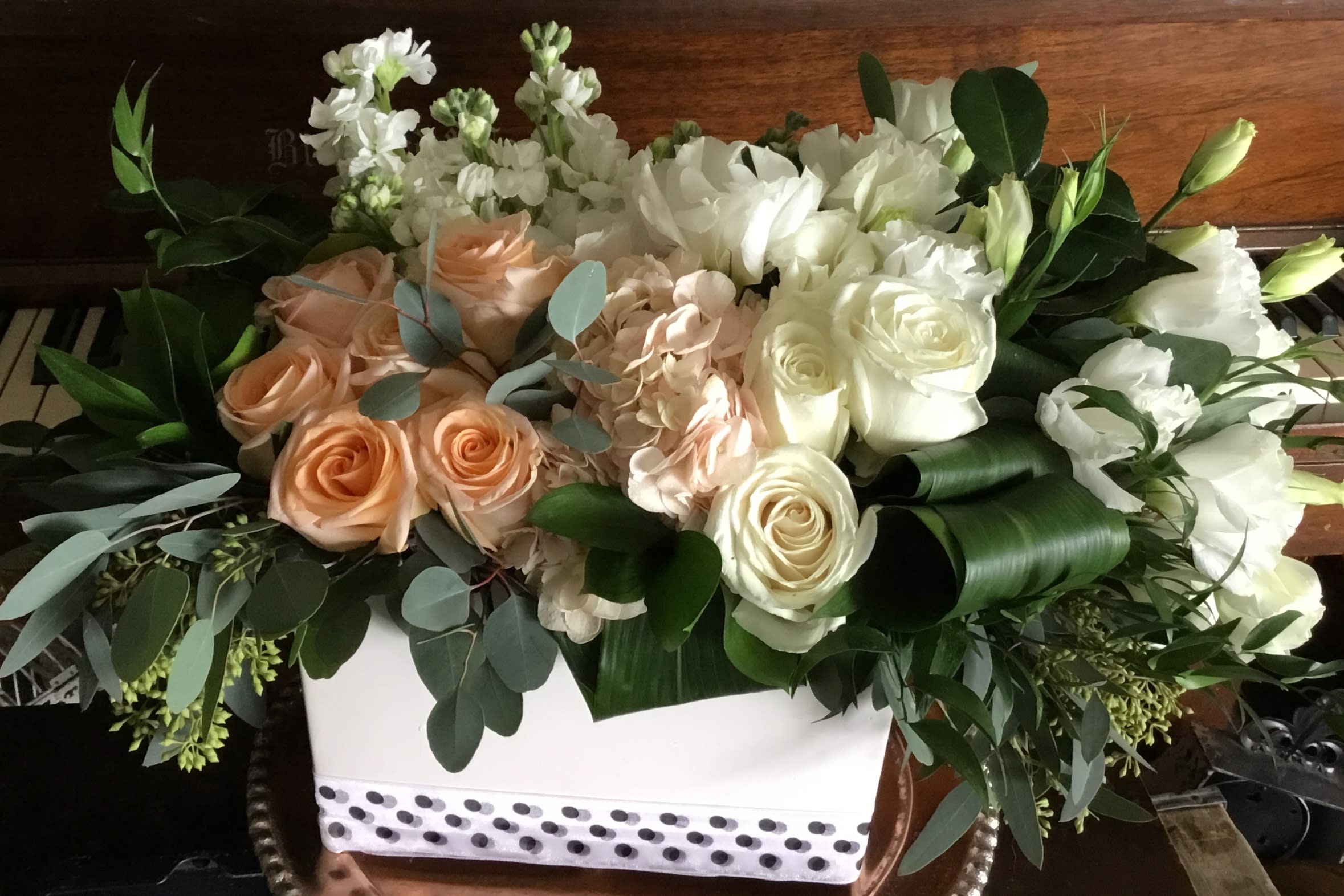 White and peach roses arranged in a white box with greenery