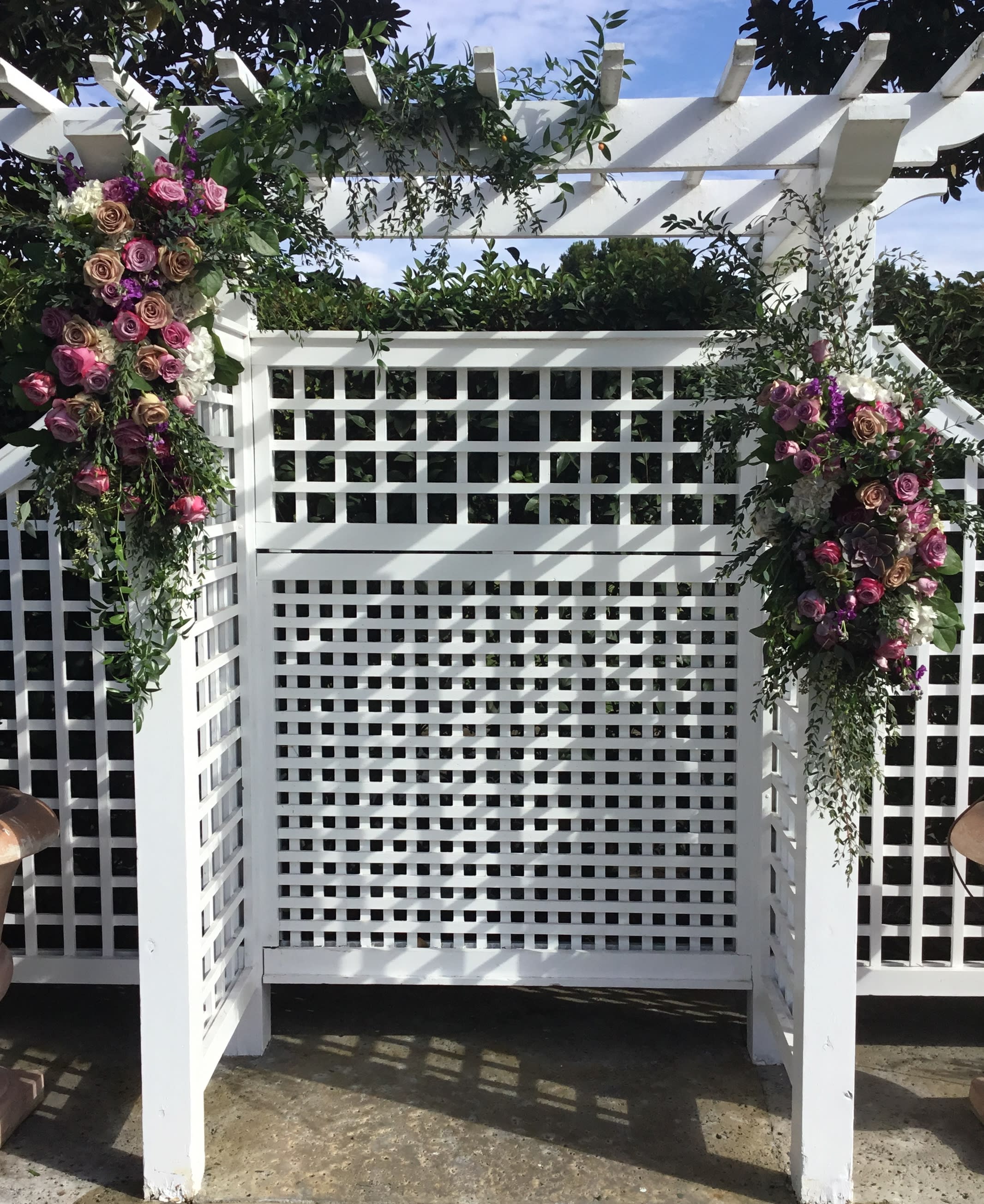 Floral arrangements of pink and purple roses on a white pergola arch