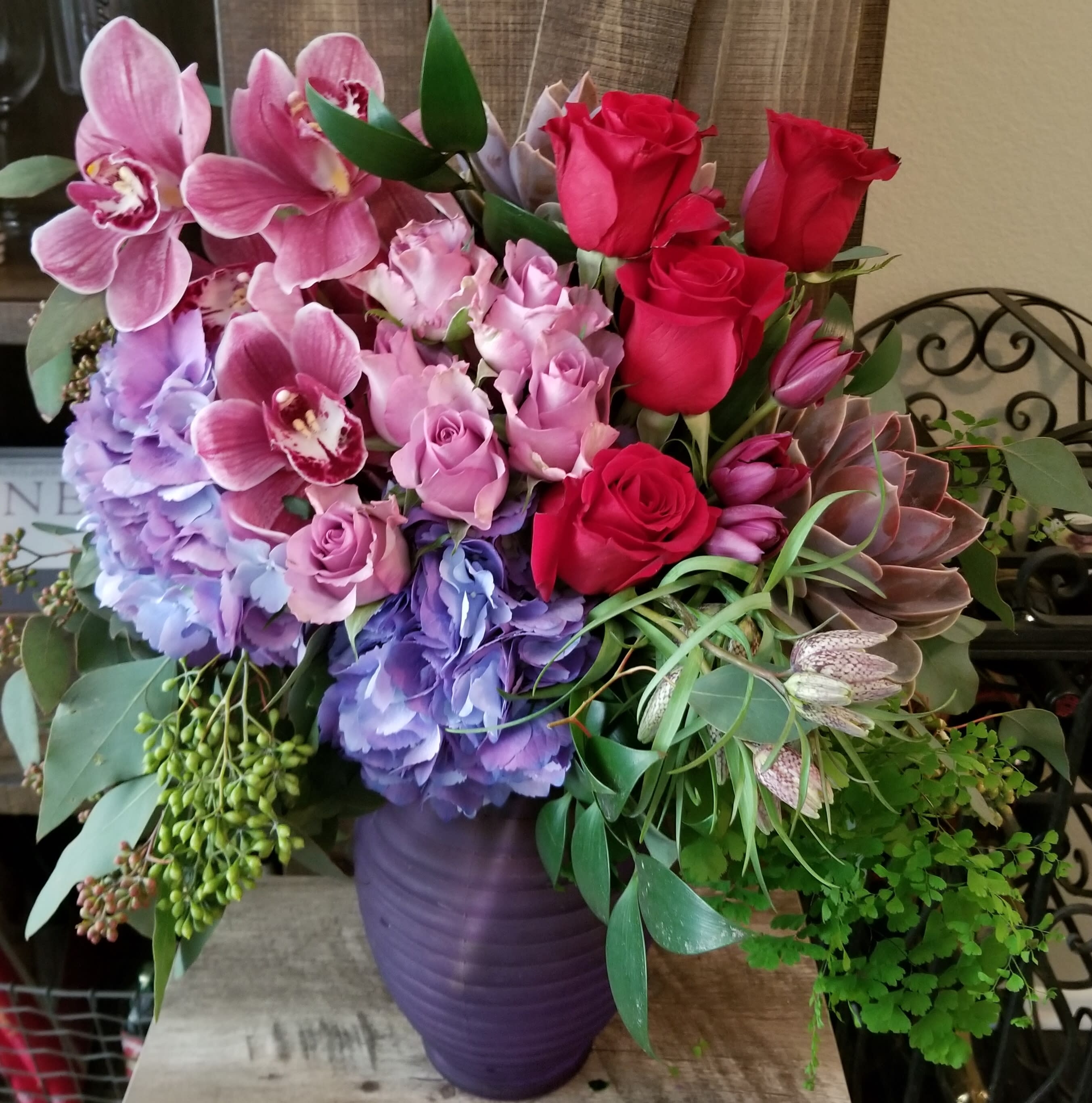 Bouquet of pink orchids, roses, hydrangeas, and succulents in a purple vase
