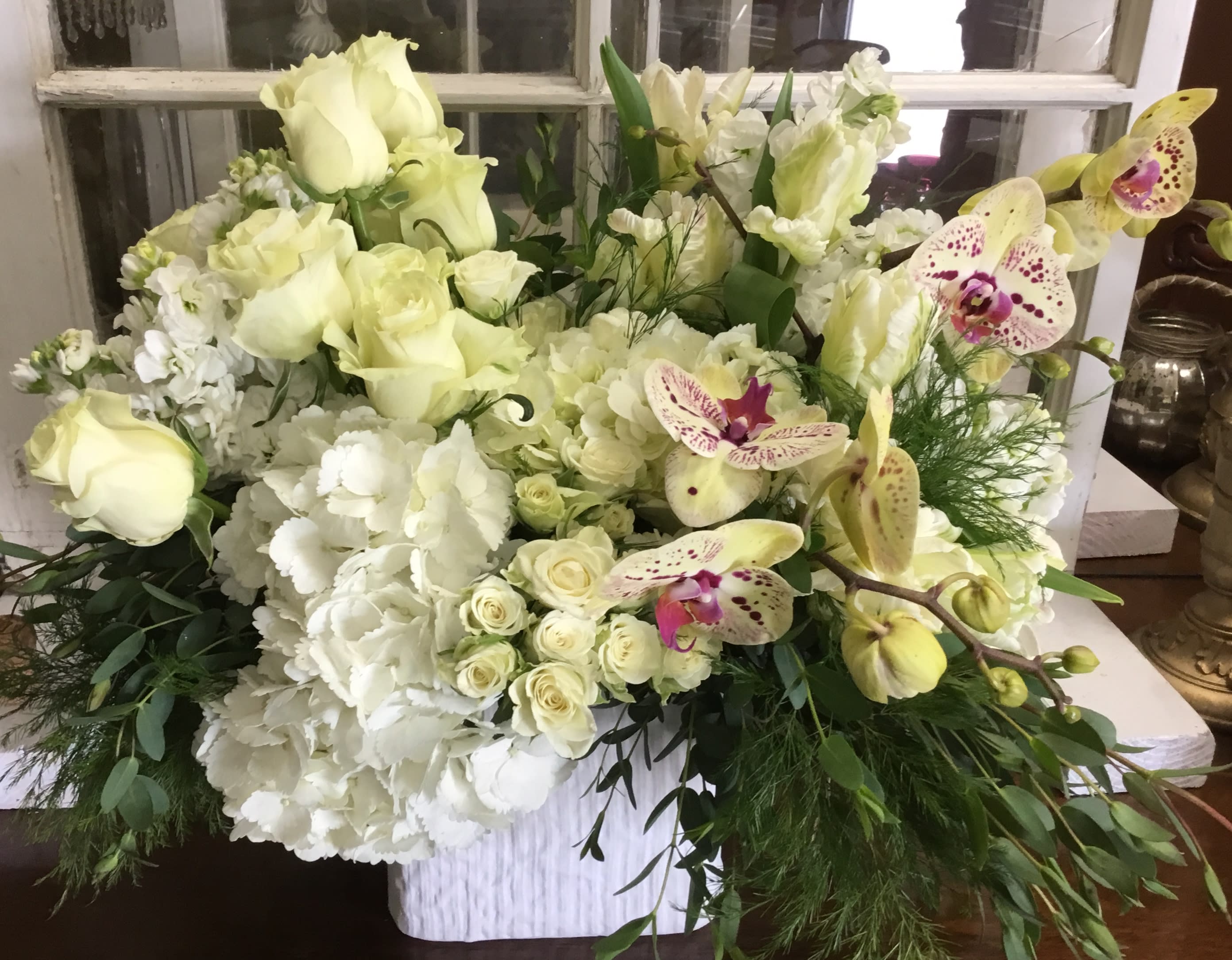 Large white floral arrangement with roses, orchids, and hydrangeas in a white container