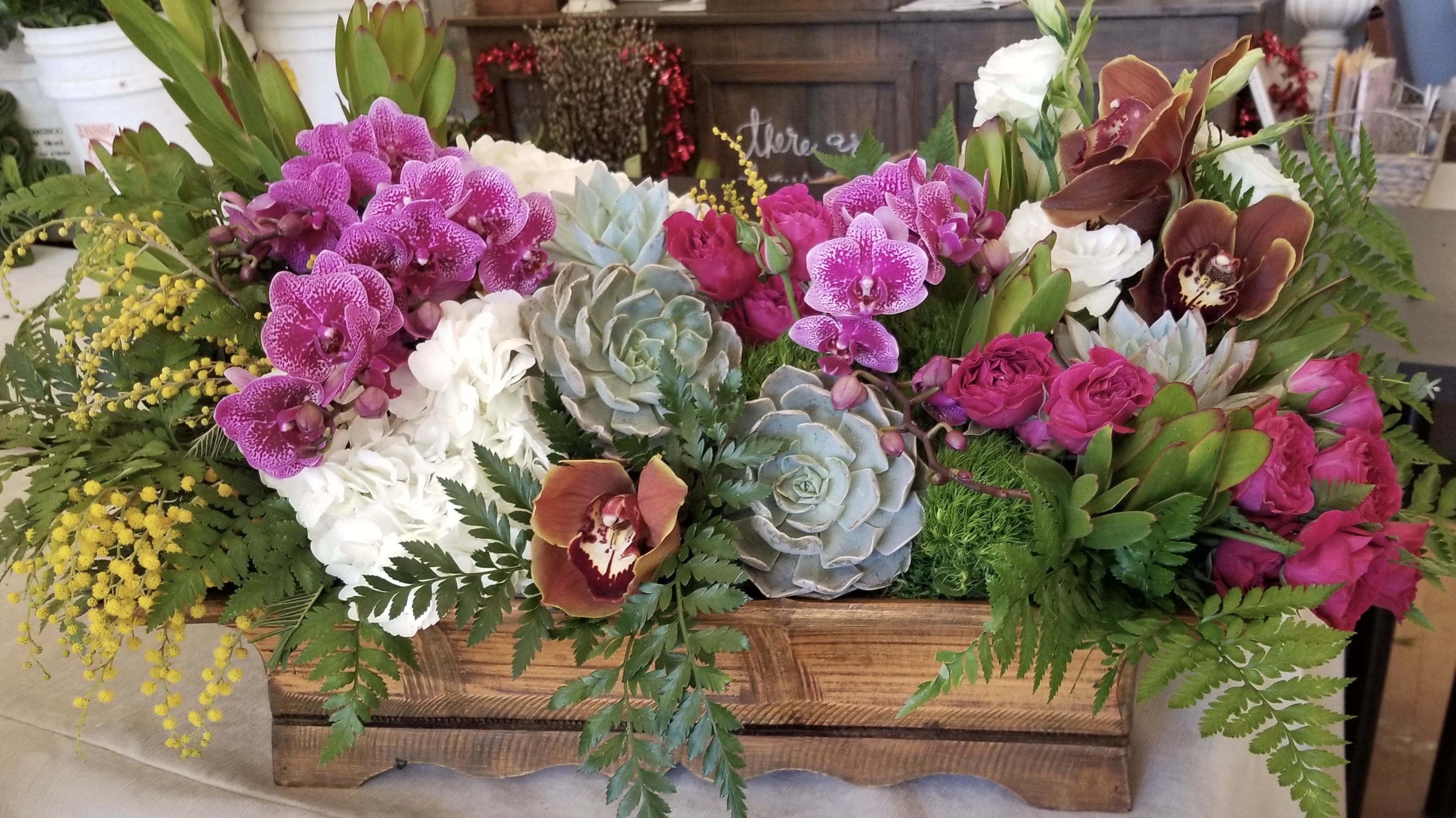 Mixed floral arrangement in a wooden box with orchids, roses, and succulents