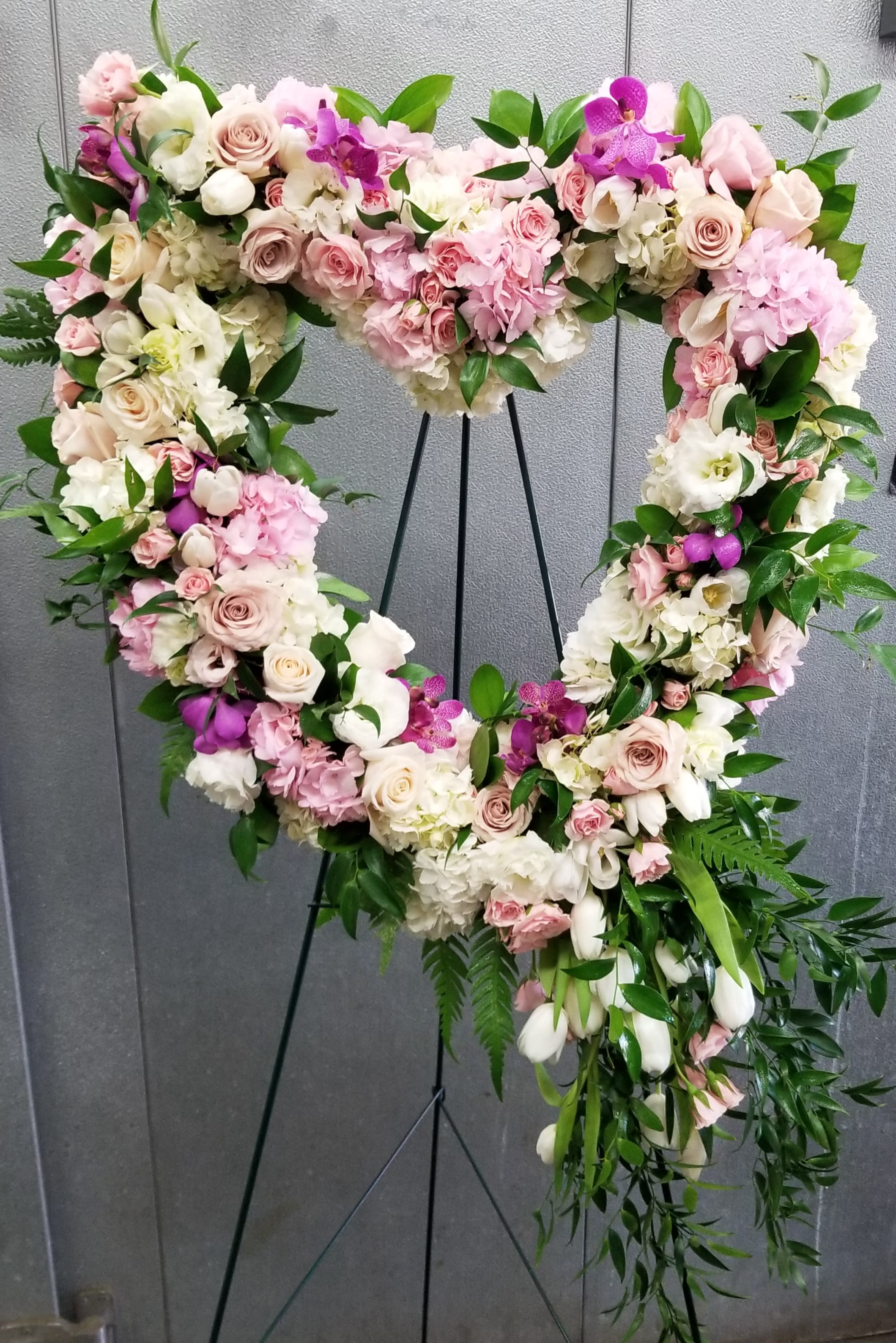 Heart-shaped floral wreath with pink and white roses on a stand