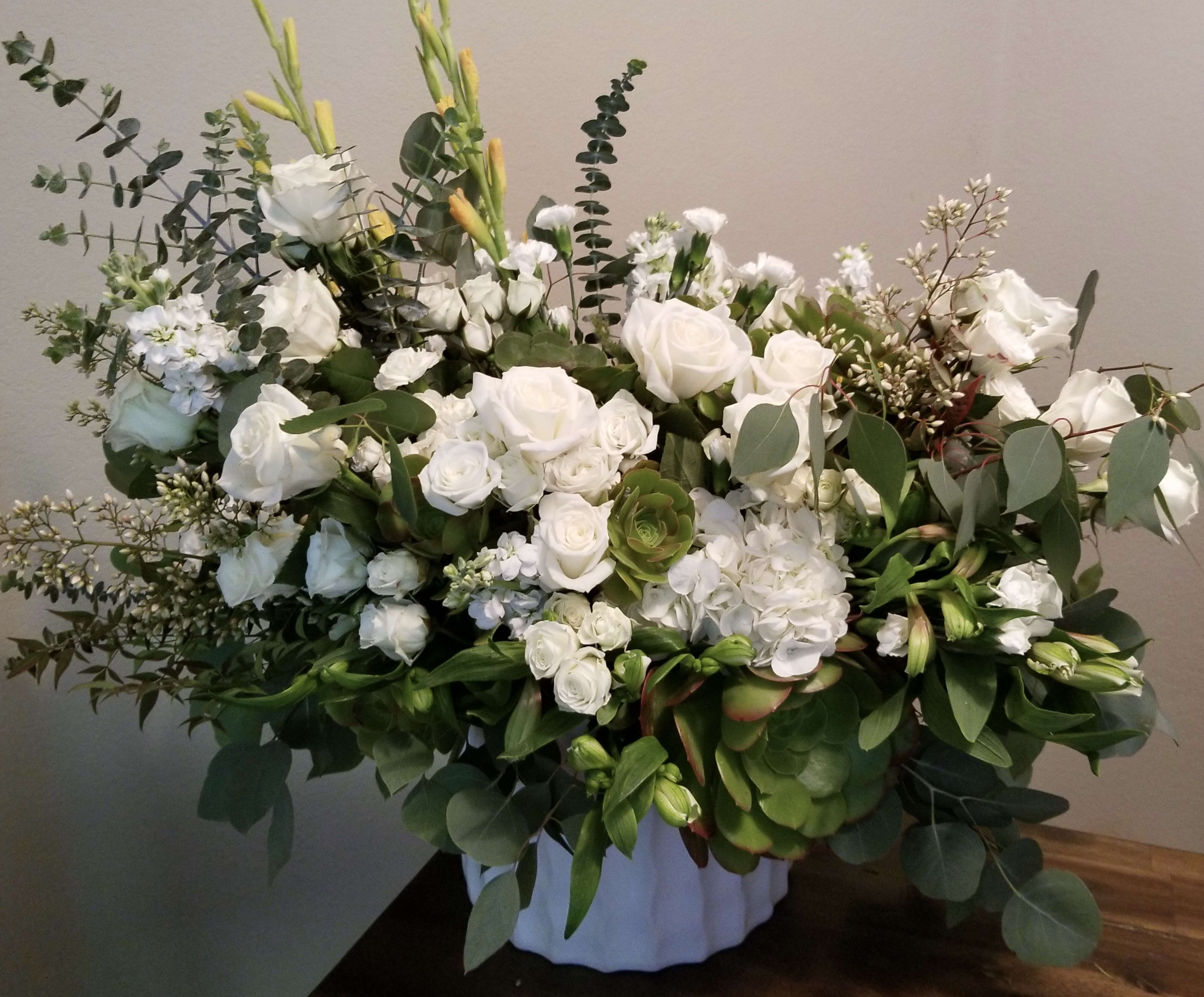 White rose arrangement in a white container with eucalyptus and greenery
