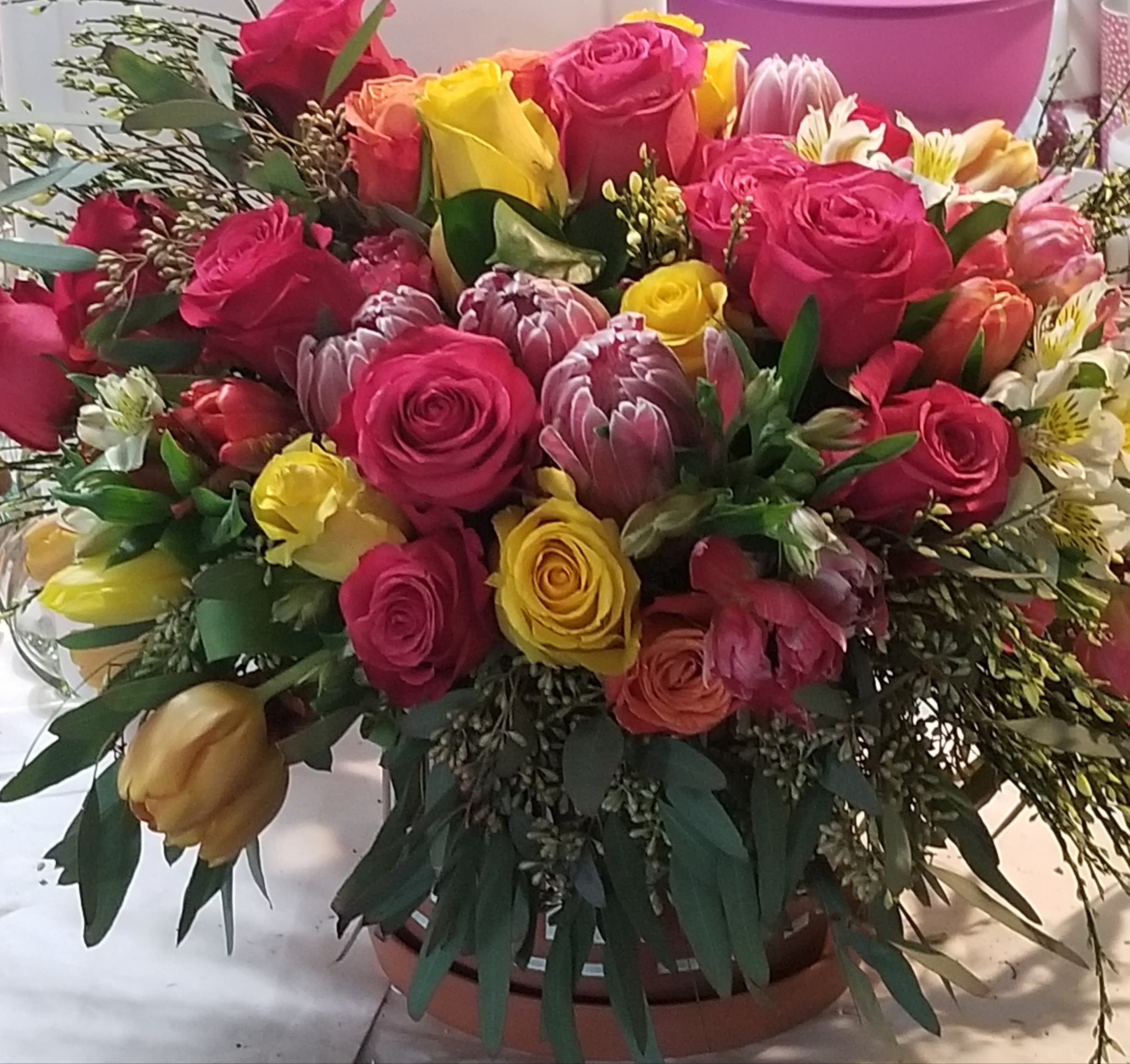 Mixed bouquet of pink and yellow roses with assorted blooms in a round container