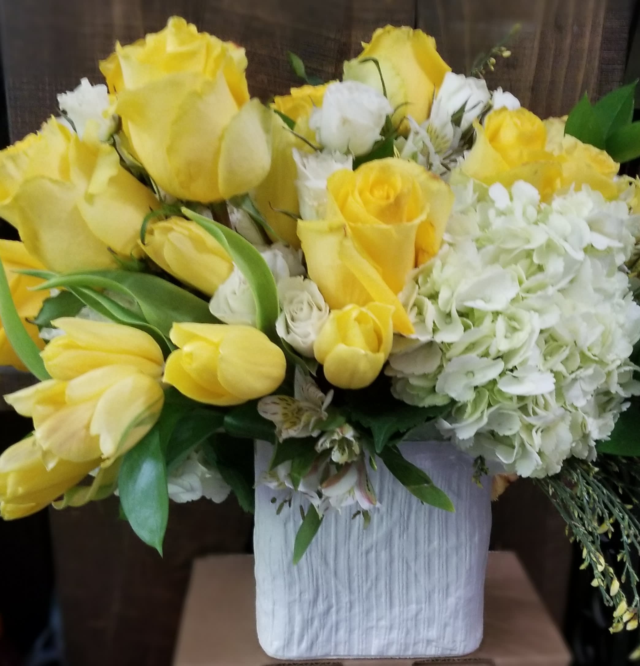 Yellow roses and white hydrangeas arranged in a white vase