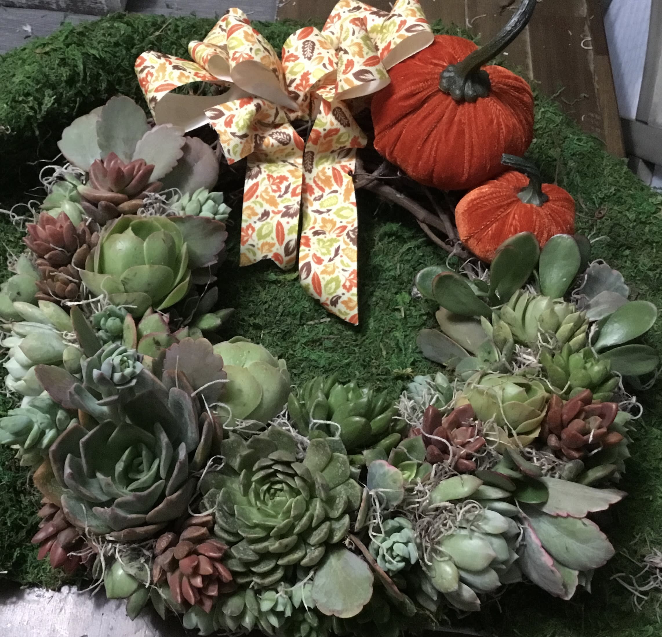 Succulent wreath with two orange pumpkins and a patterned bow