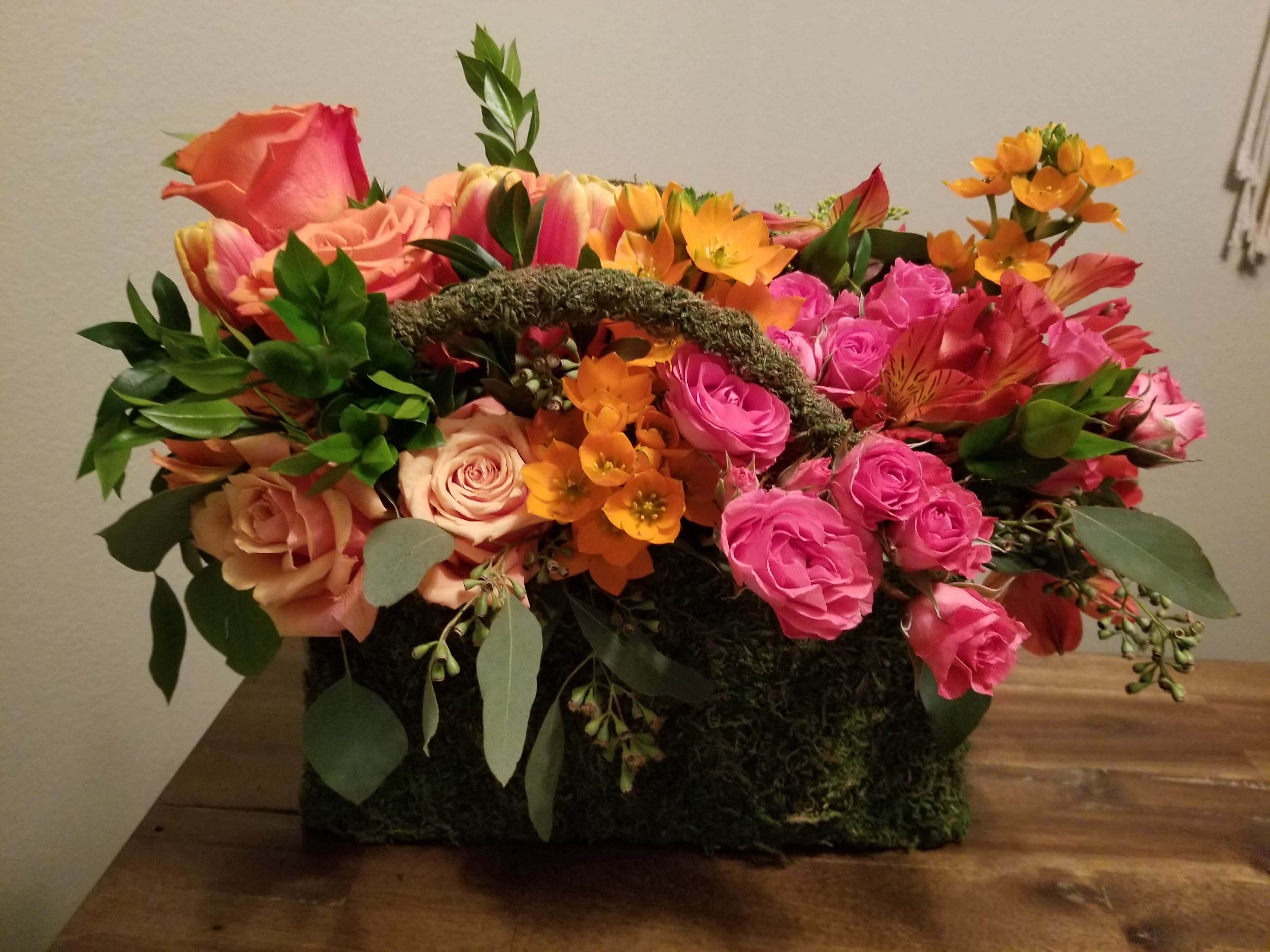 Mixed bouquet of pink and orange roses in a moss-covered basket