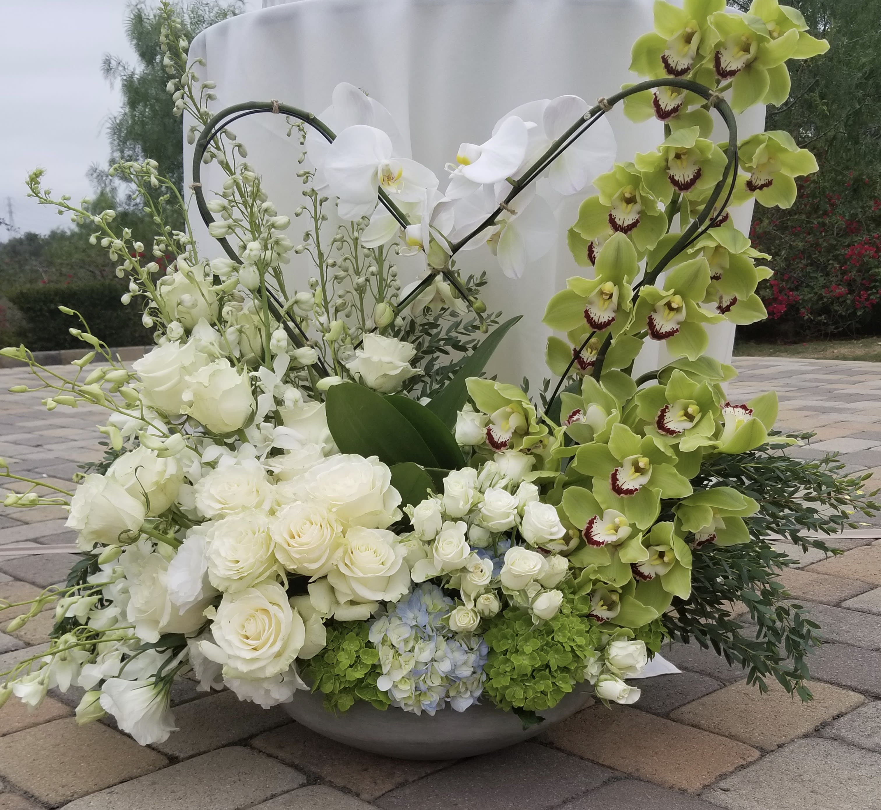 Large floral arrangement with white roses and green orchids in a low bowl