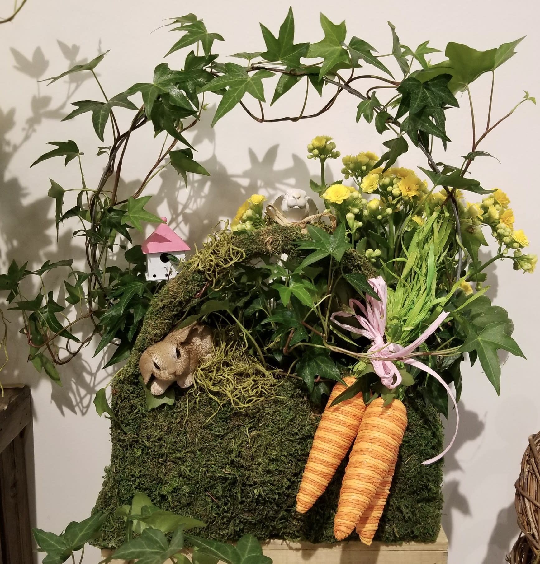 Moss-covered arrangement with yellow flowers, ivy, and two orange carrots
