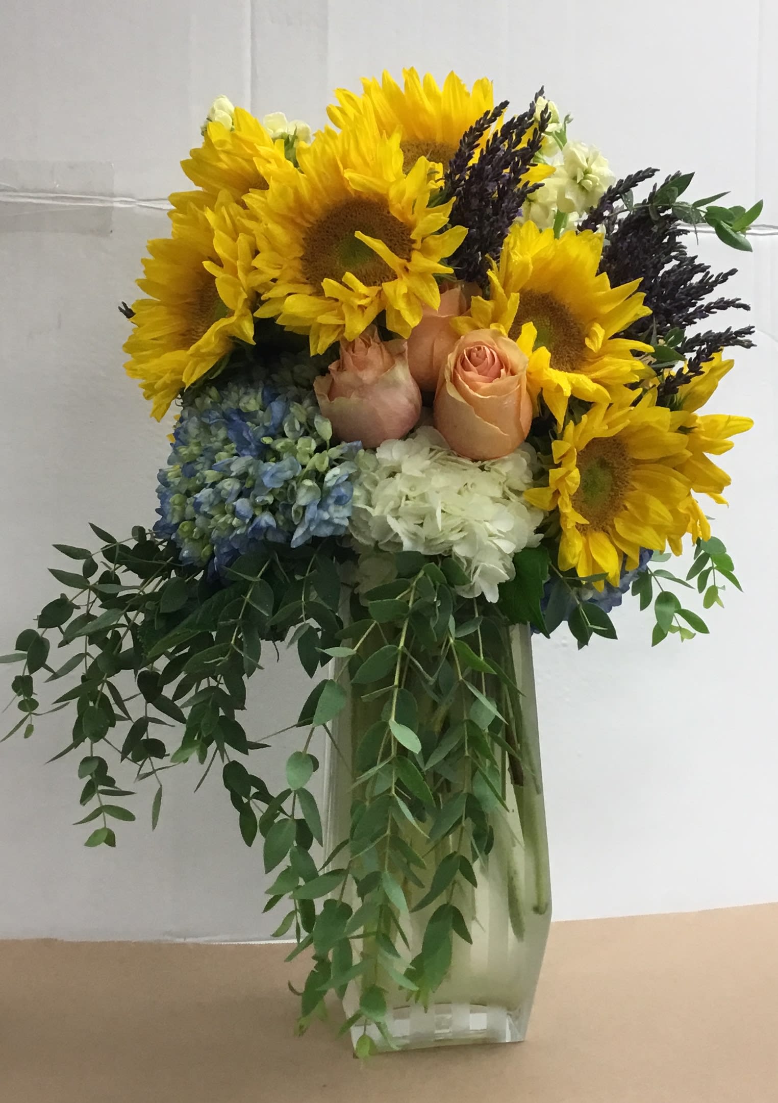 Sunflower and rose arrangement in a clear vase with trailing greenery